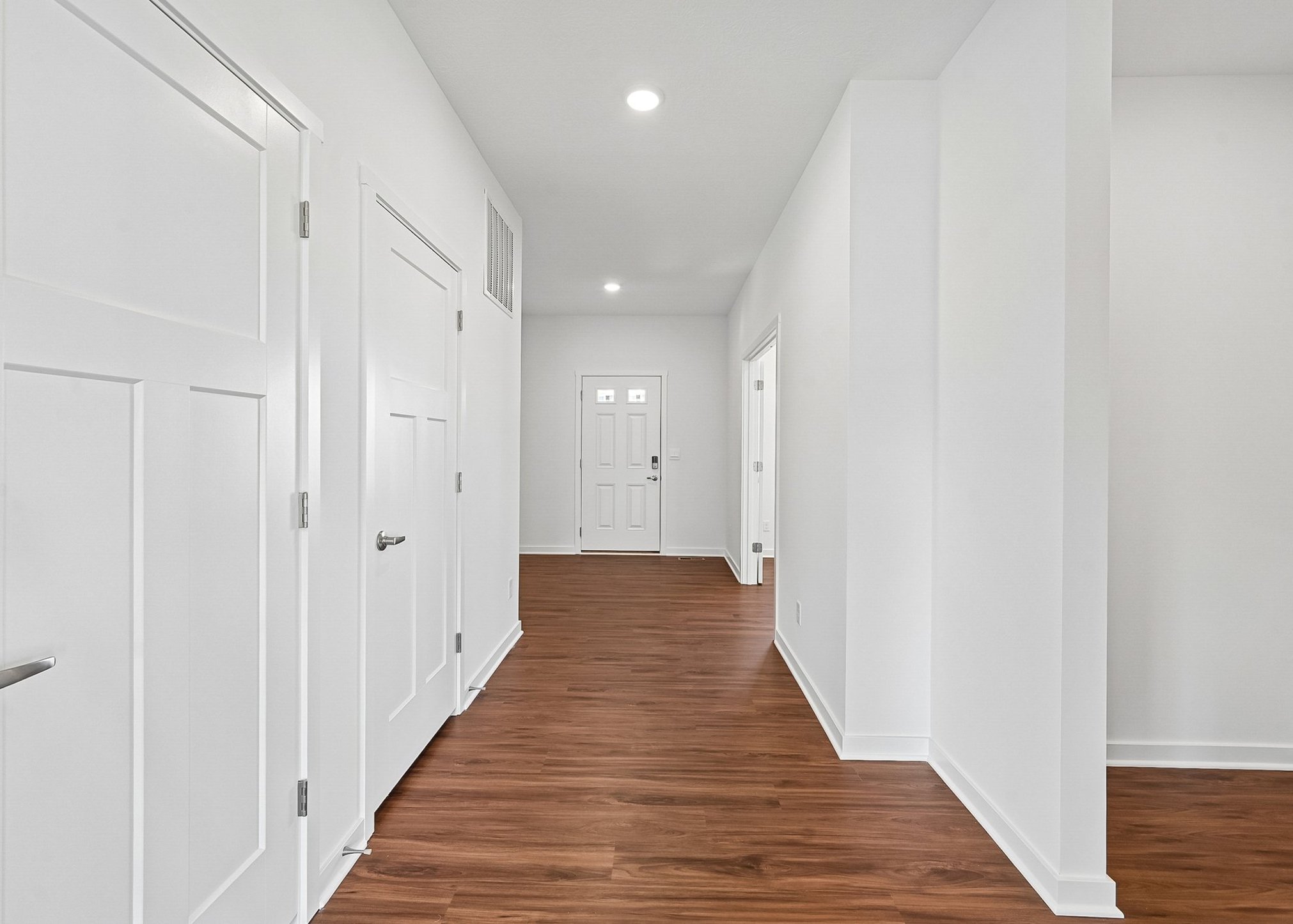 A bright hallway with white walls, wooden flooring, and several doors leading to different rooms.