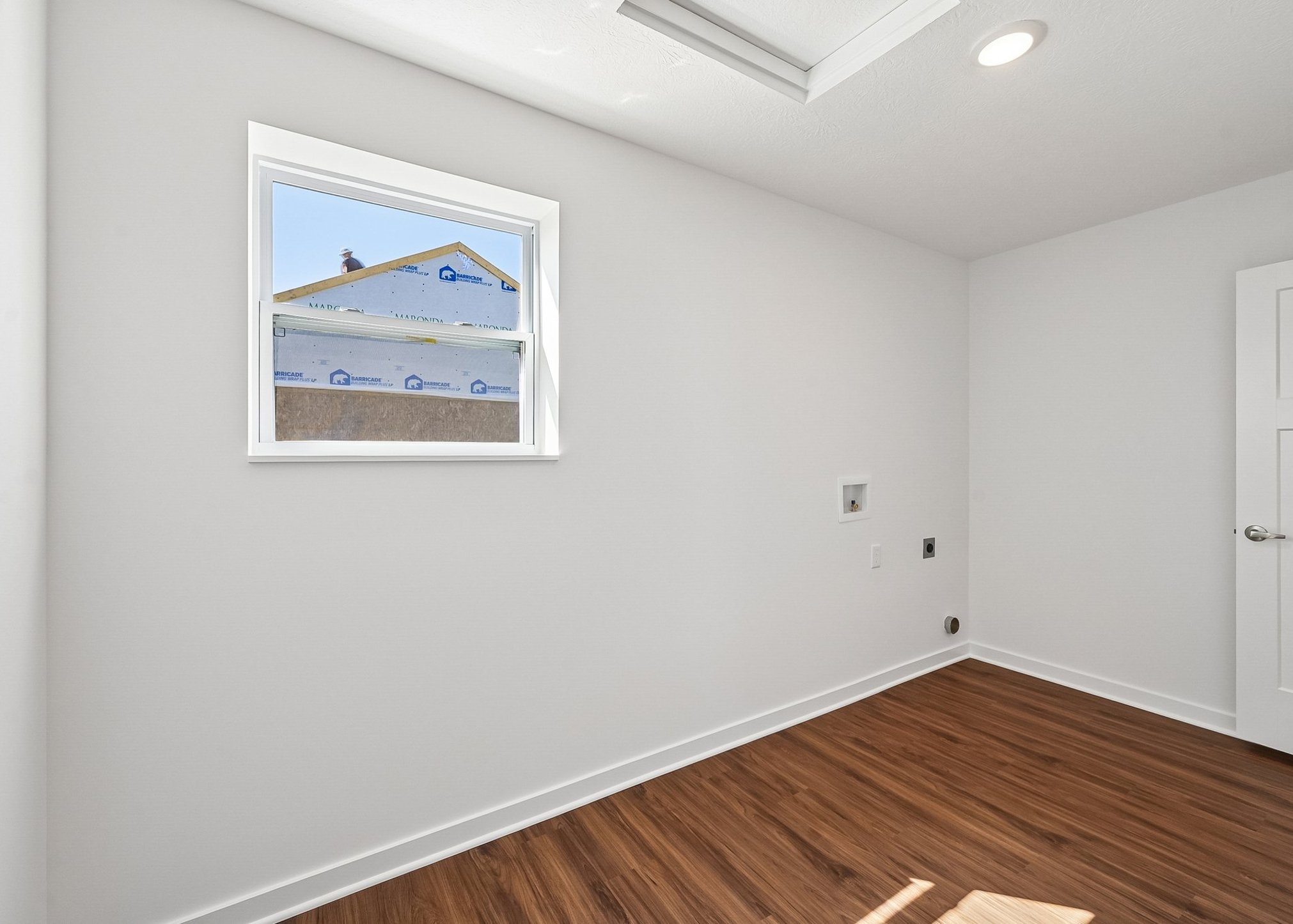 Bright, empty room with a window showing a construction site outside and wooden flooring.