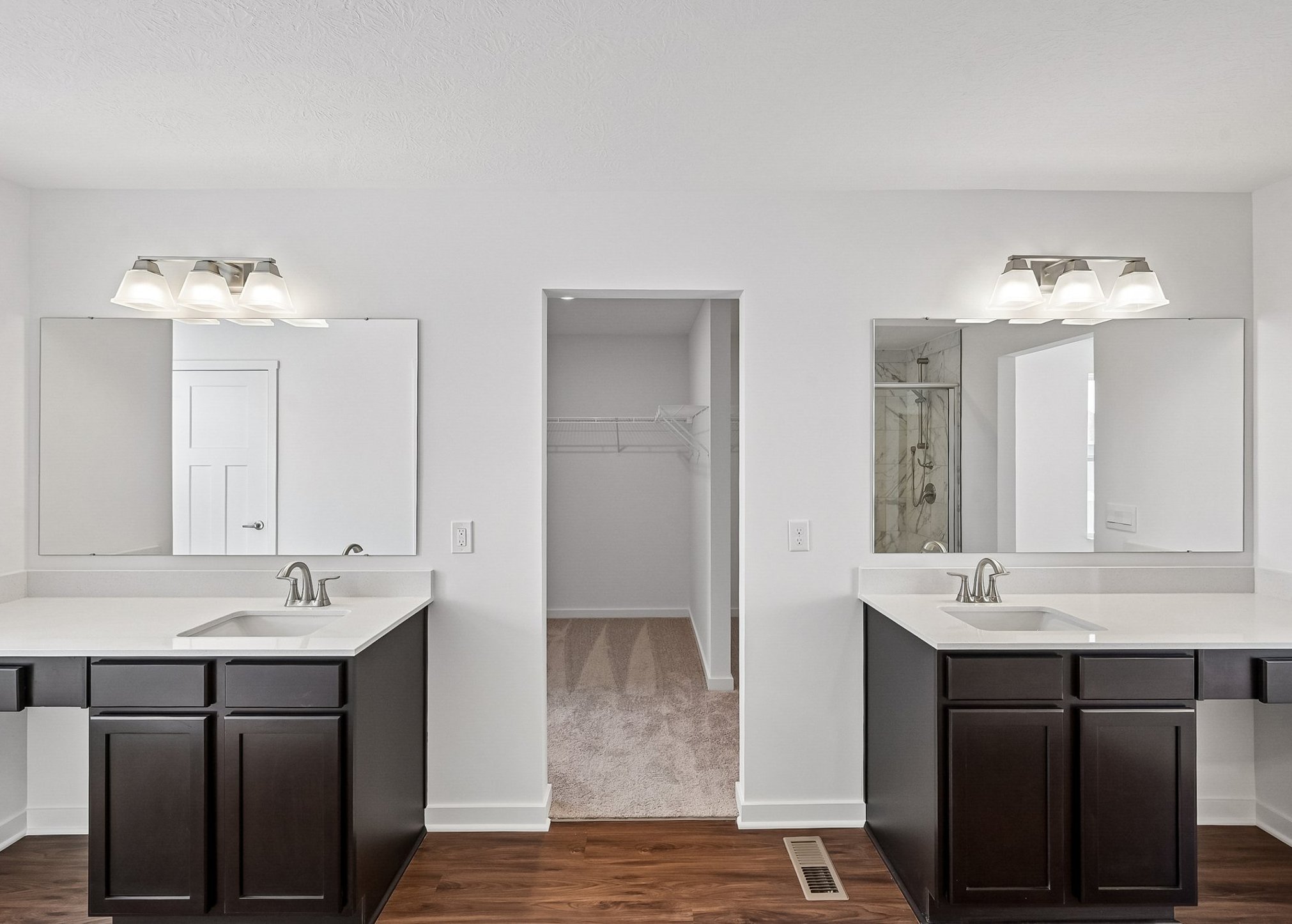 Dual sink vanity with mirrors in a modern bathroom featuring light-colored walls and wood flooring.