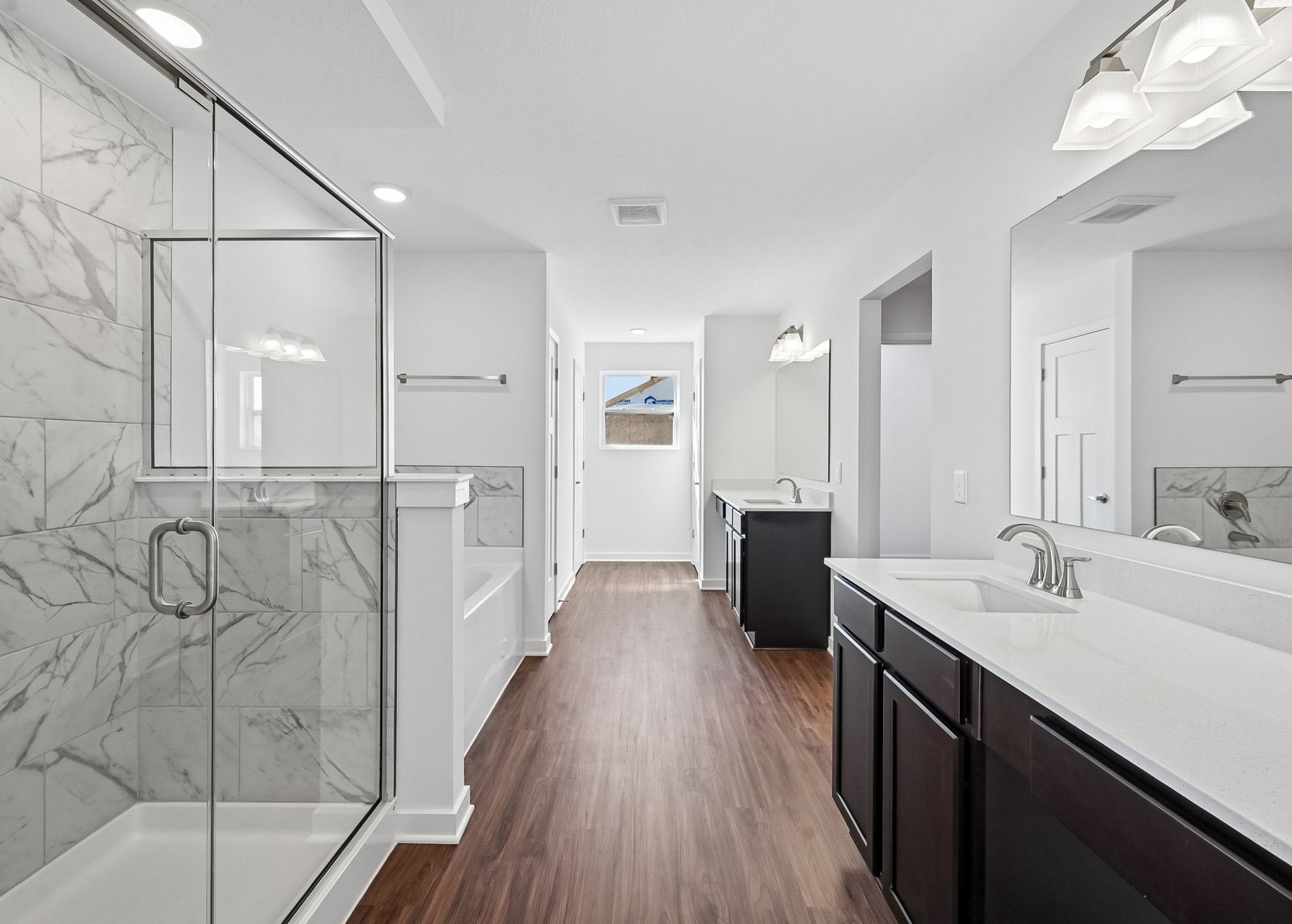 Spacious modern bathroom featuring a glass shower, double sinks, and natural light from a window.