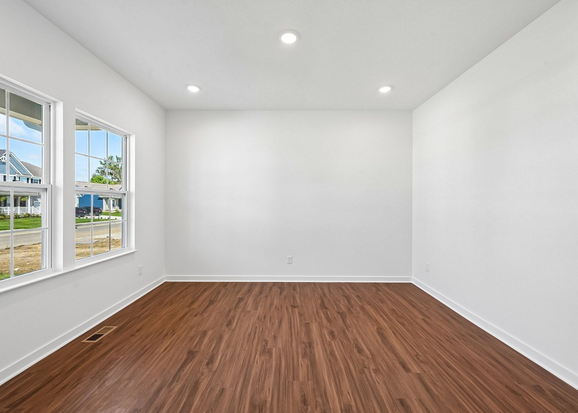 Bright, empty room with light hardwood flooring and large windows.