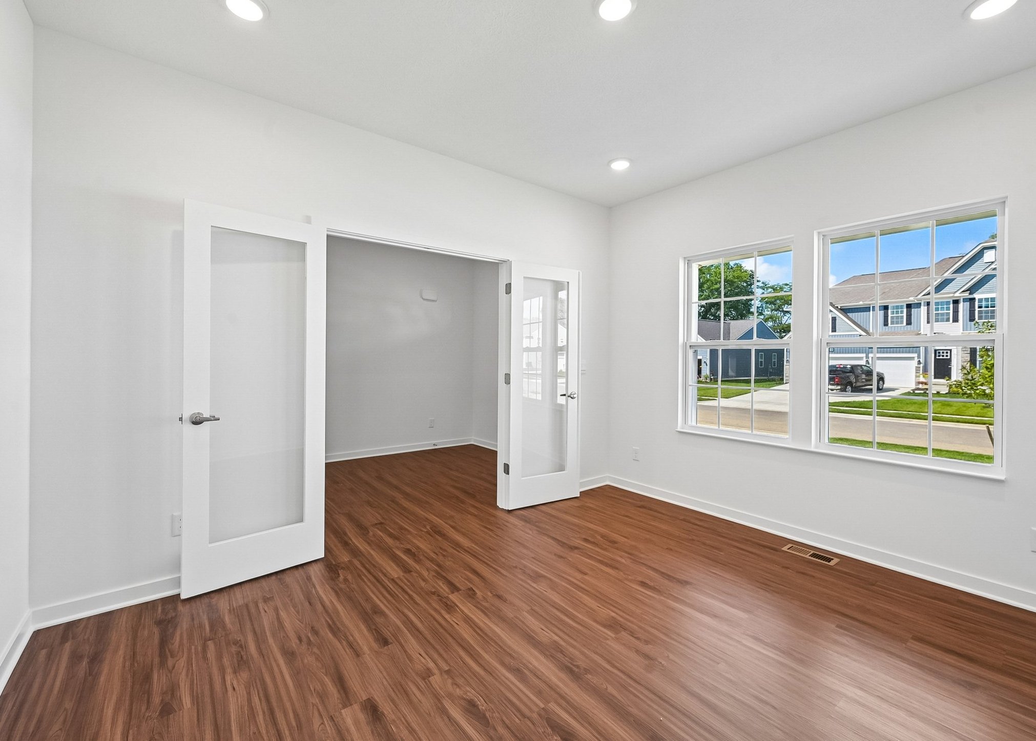 Bright, airy room with wooden flooring, featuring large windows and double doors leading to another space.