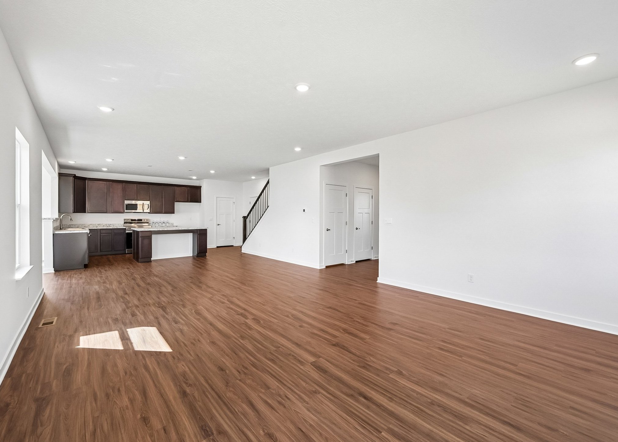Spacious, empty living area with wood laminate flooring and modern kitchen in the background.