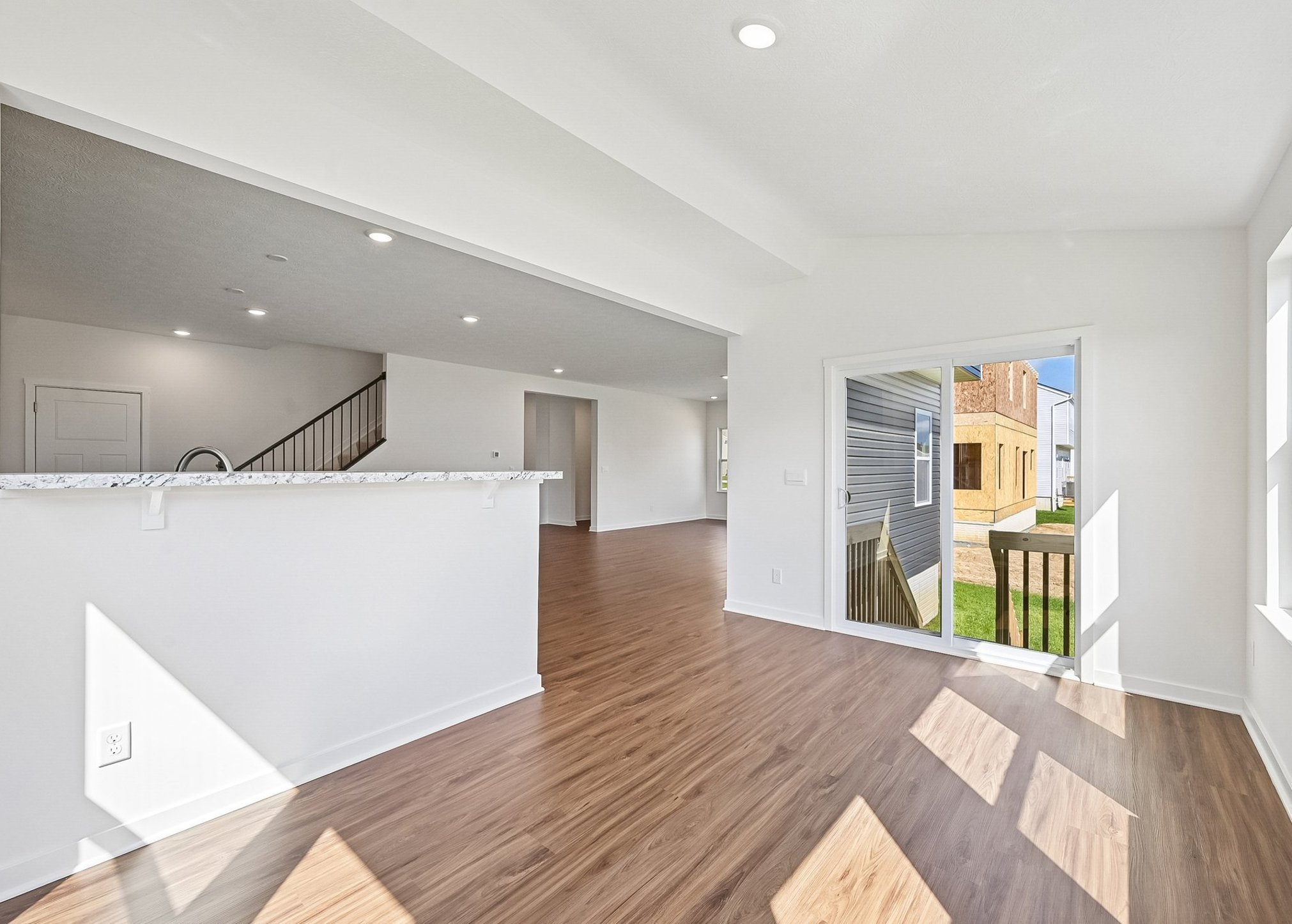 A bright, modern interior view of an open-concept living space with a wooden floor and large windows leading to a yard.