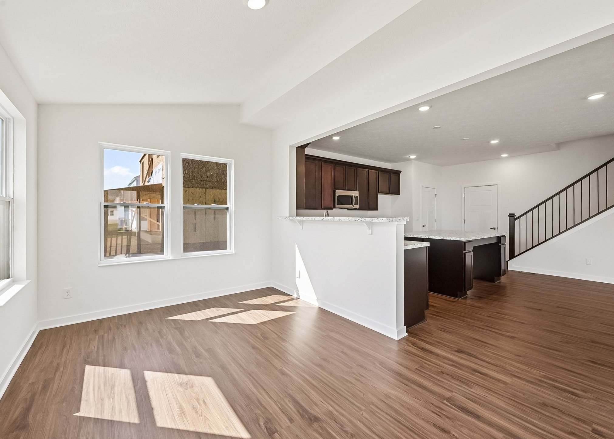 Bright, spacious living area with wood flooring and a view of the kitchen.