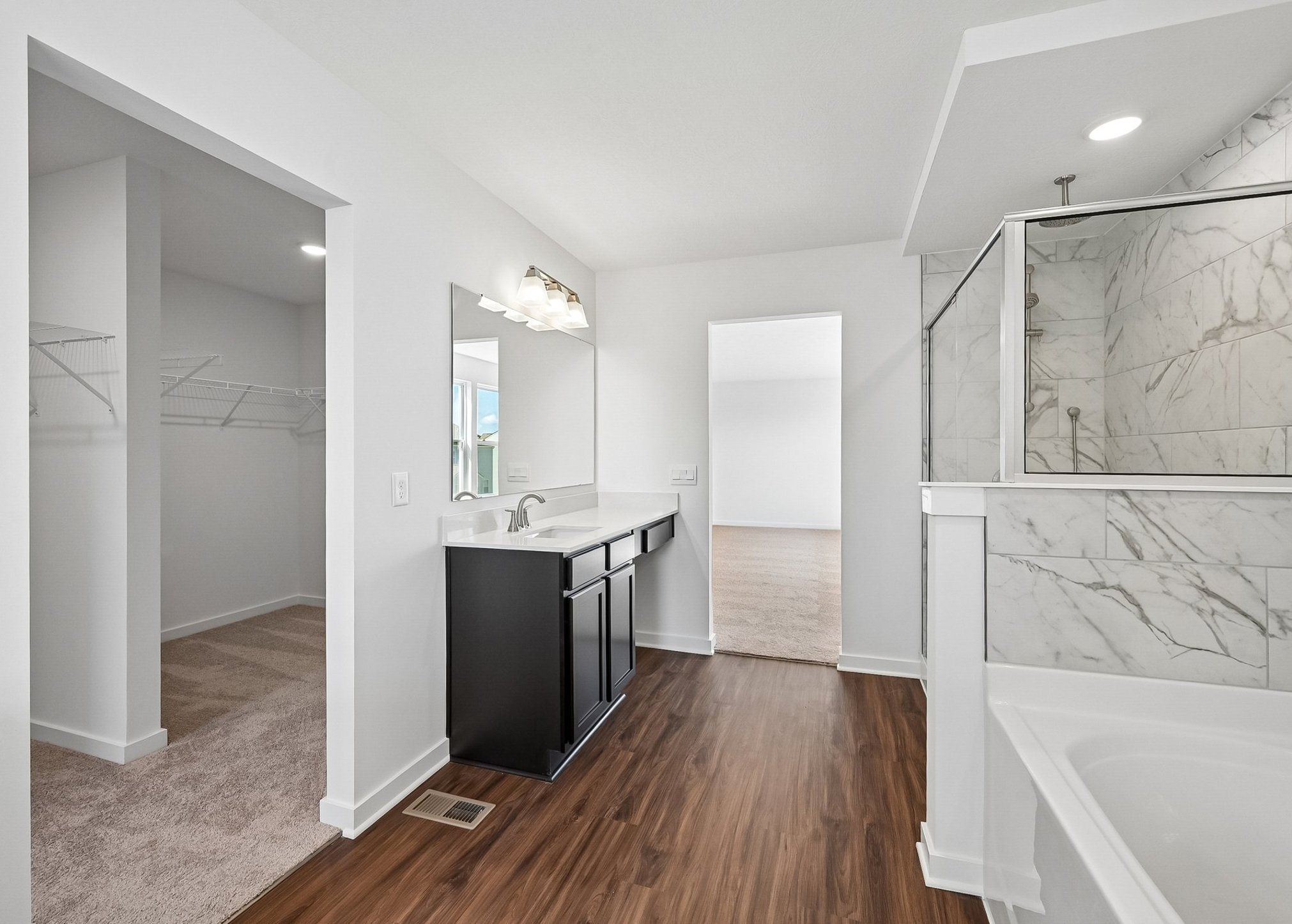 Bright bathroom featuring a black vanity, large mirror, and a separate shower with marble tile.