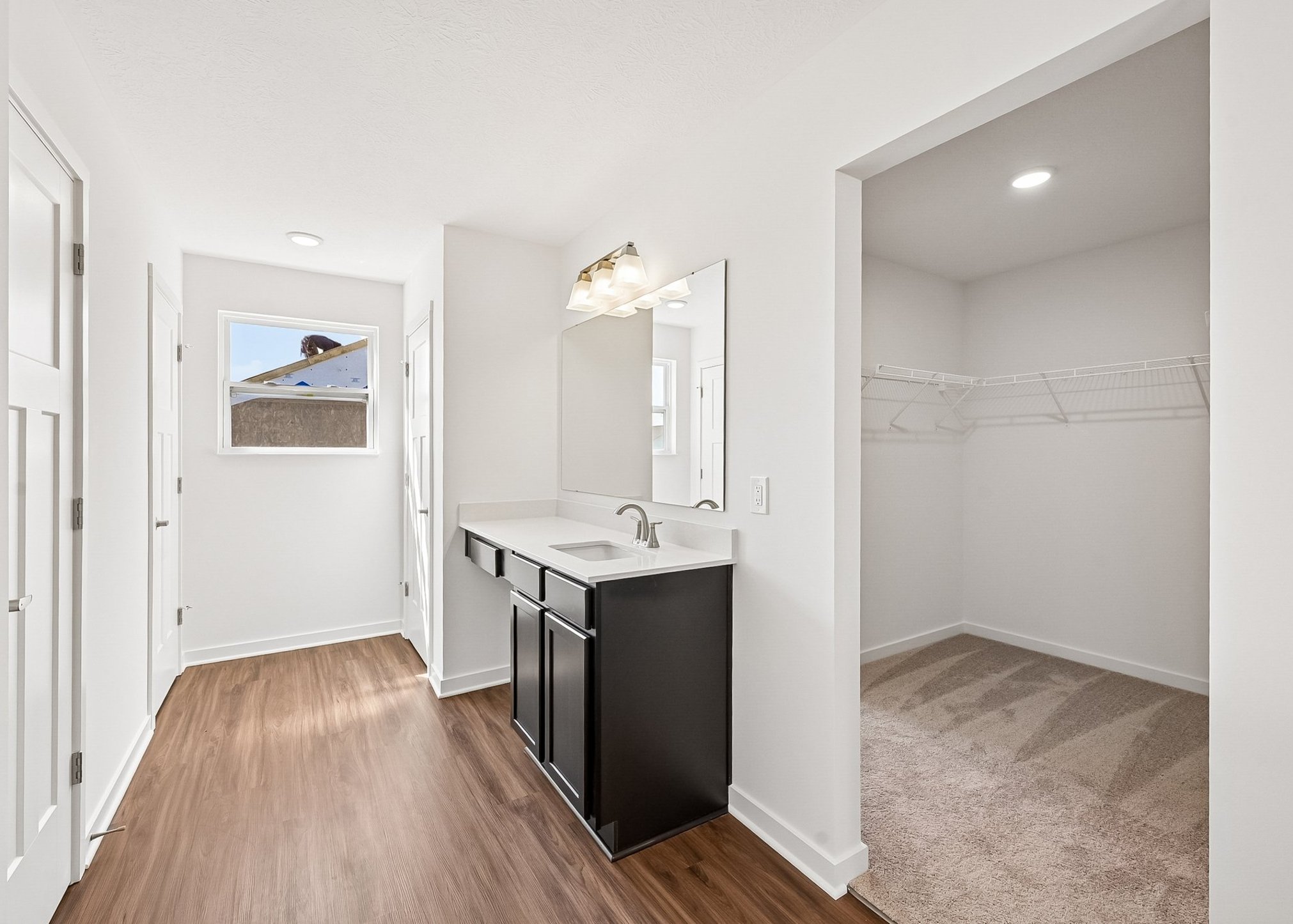 Bright hallway leading to a bathroom vanity with a mirror, and a closet with open shelving.