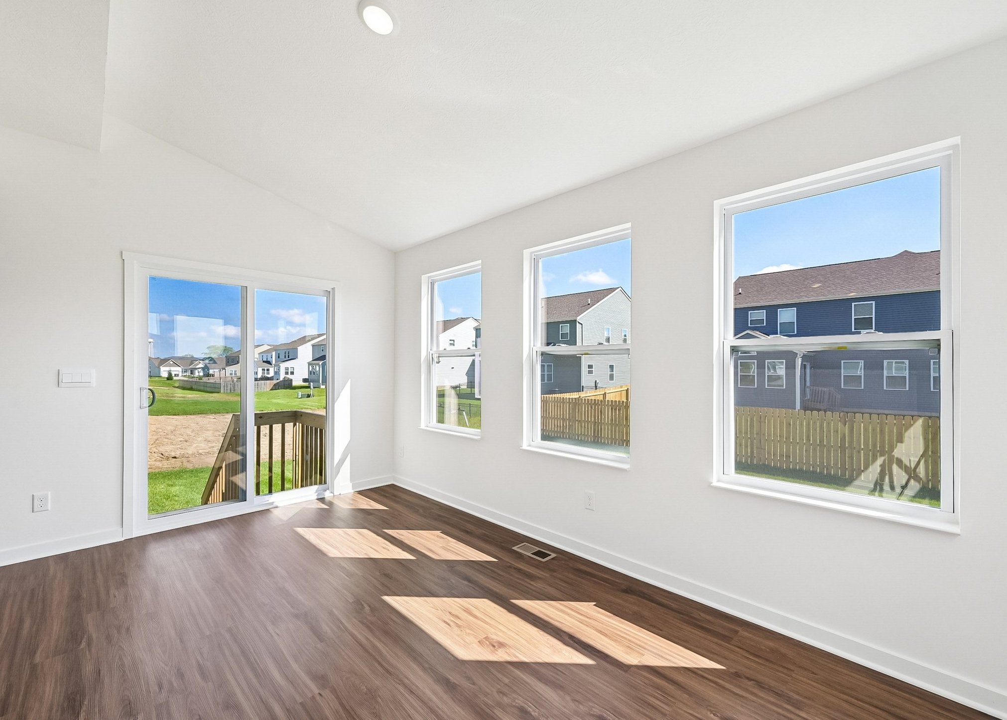 Bright room with large windows, wooden floor, and a sliding glass door leading to an outdoor area.