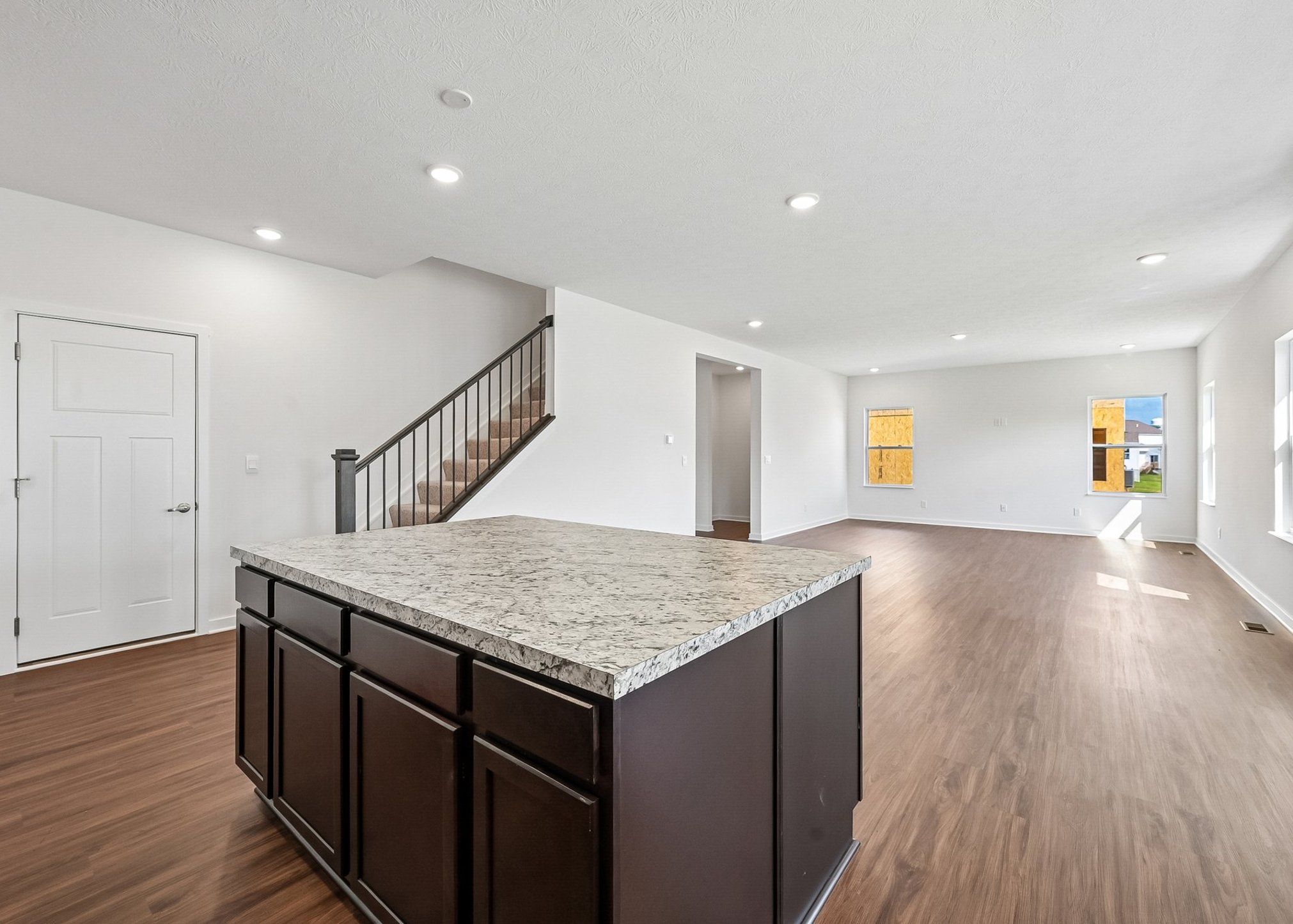 Open concept living space featuring a kitchen island with a granite countertop and hardwood floors, leading to well-lit, empty rooms.