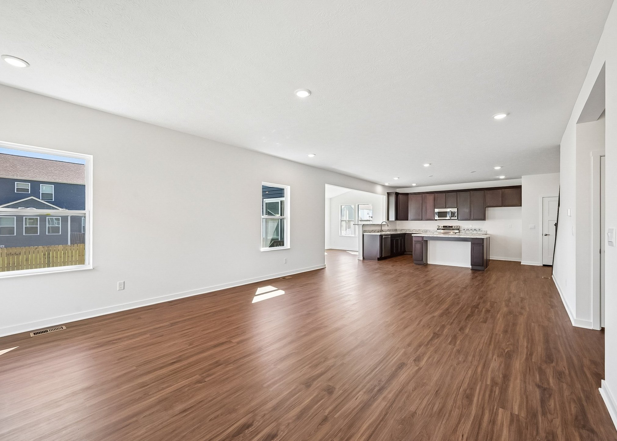 Bright, spacious living area with wooden flooring and open kitchen layout, featuring large windows for natural light.