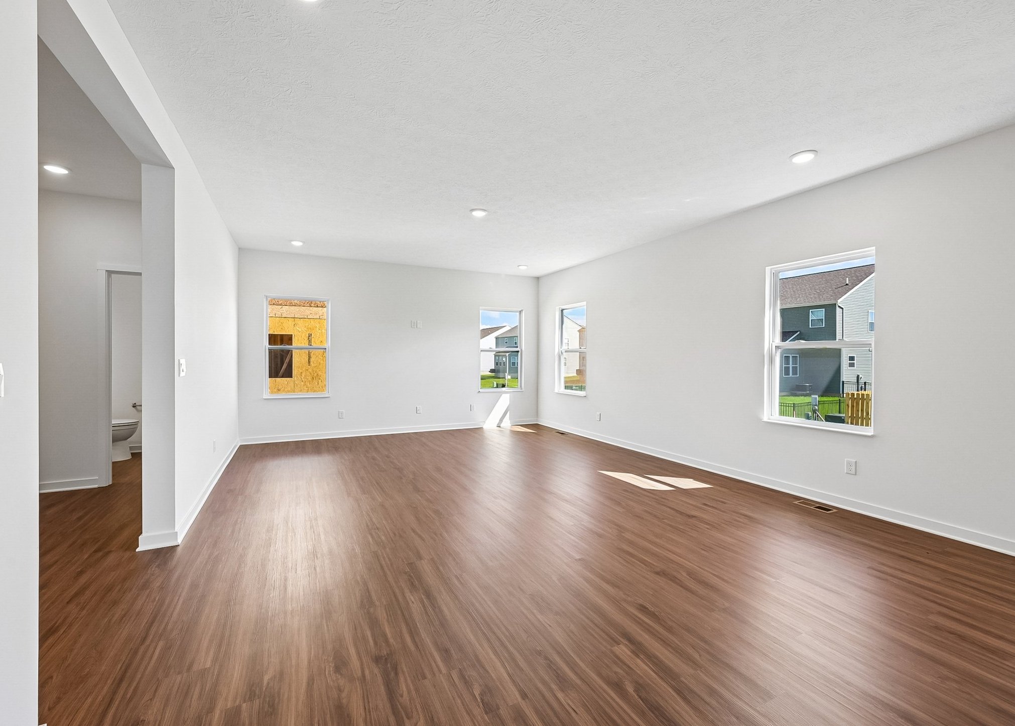 A spacious, empty room with brown laminate flooring and large windows allowing natural light.
