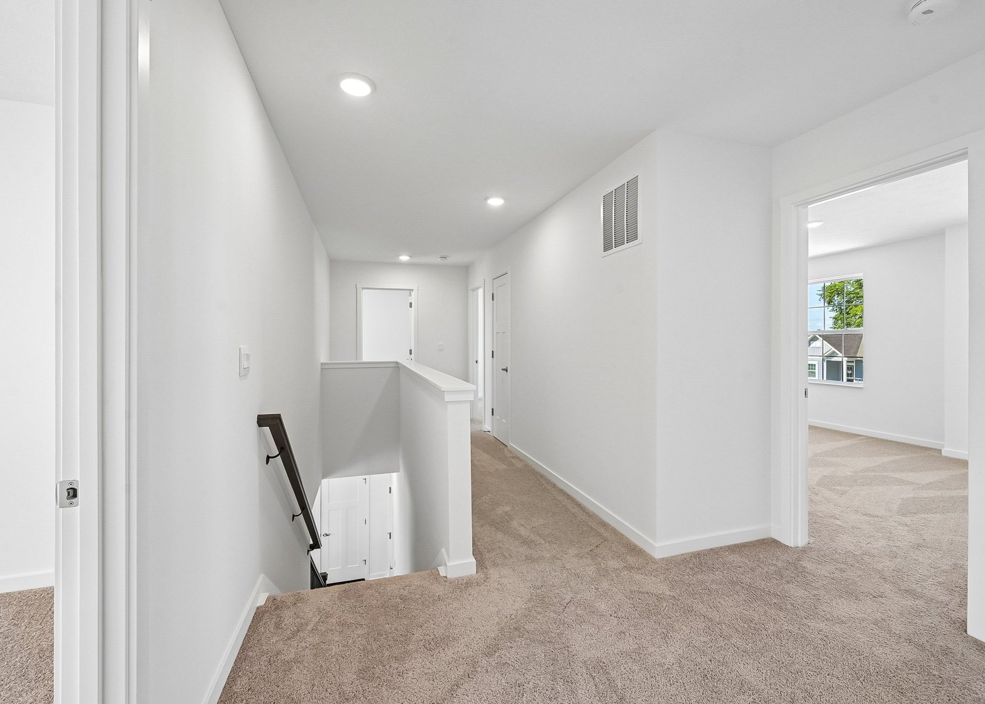 A softly lit hallway with a carpeted floor, leading to multiple rooms and a staircase.
