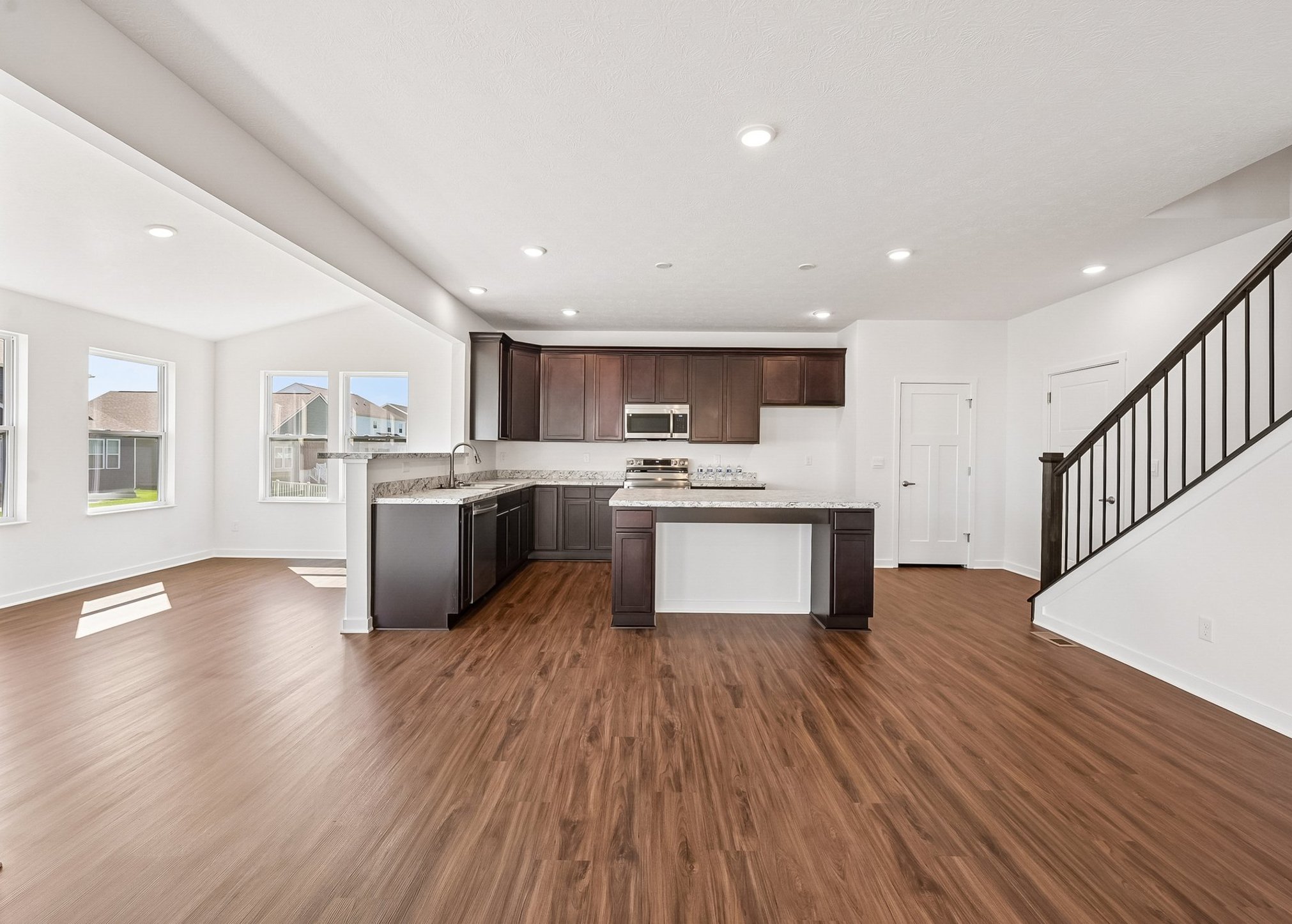 Modern kitchen with dark wood cabinets and a granite countertop, featuring an open layout with large windows and hardwood flooring.
