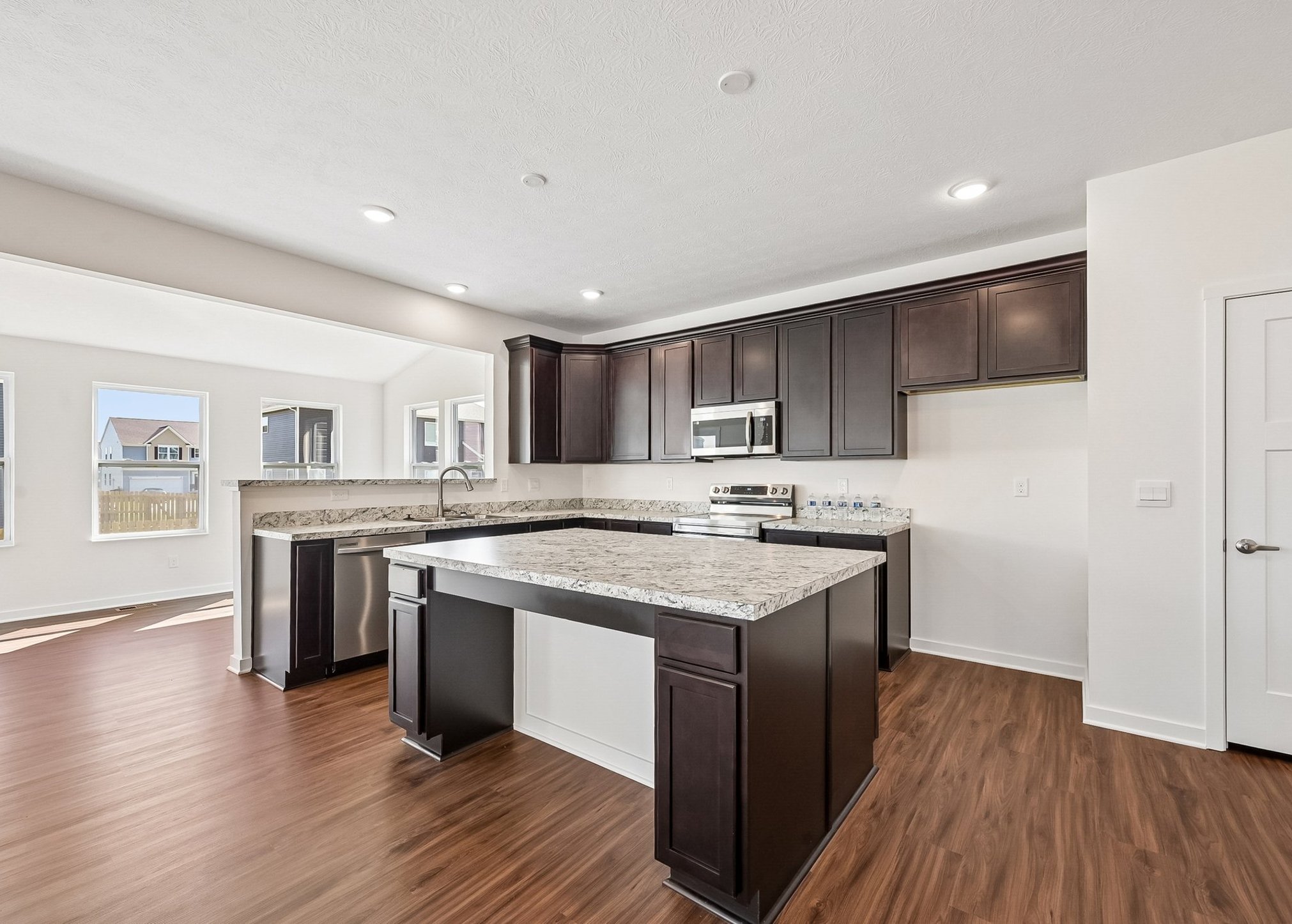 Modern kitchen featuring dark wood cabinets, a large island with granite countertops, and stainless steel appliances.