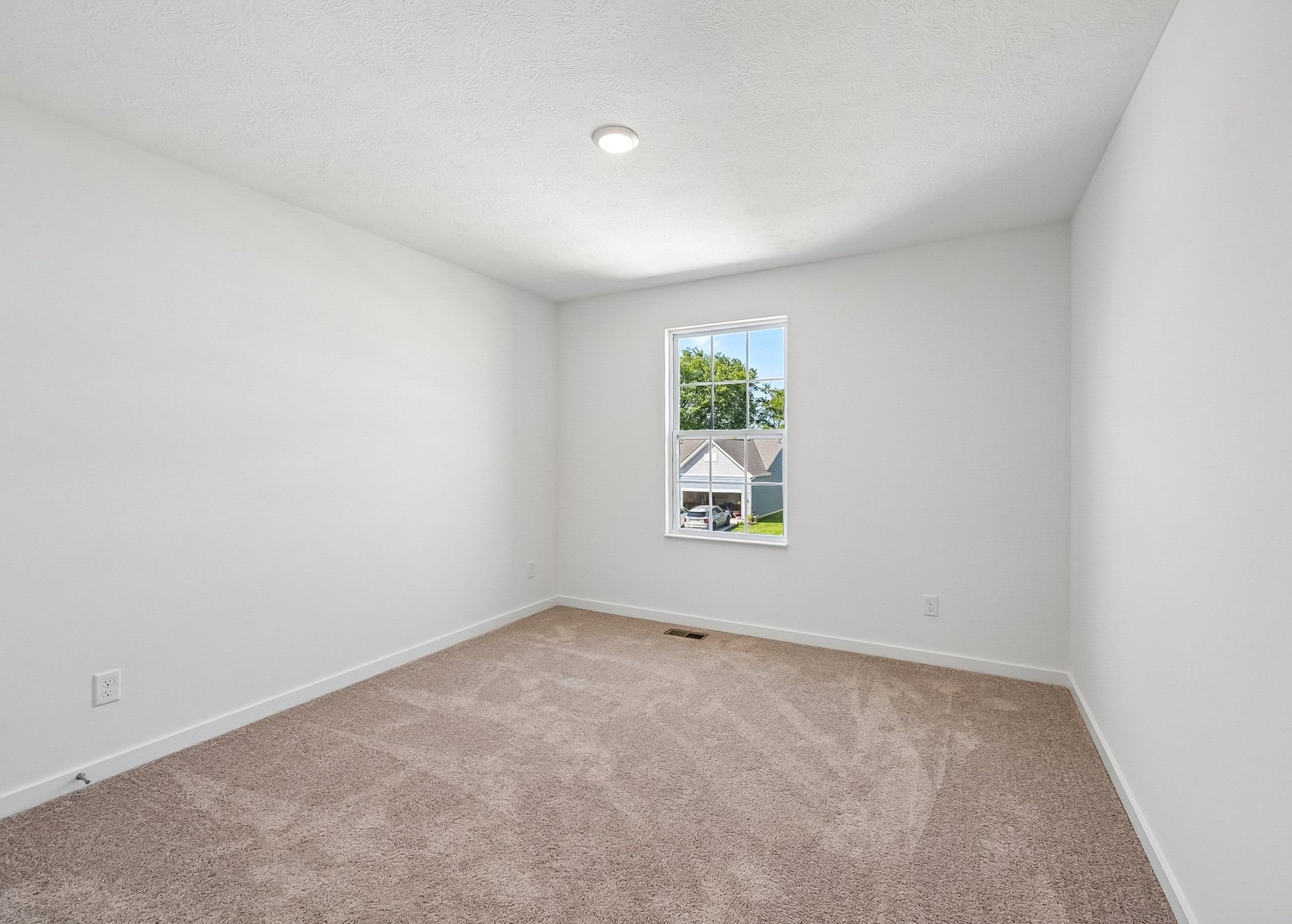 Empty room with beige carpet, white walls, and a window letting in light.