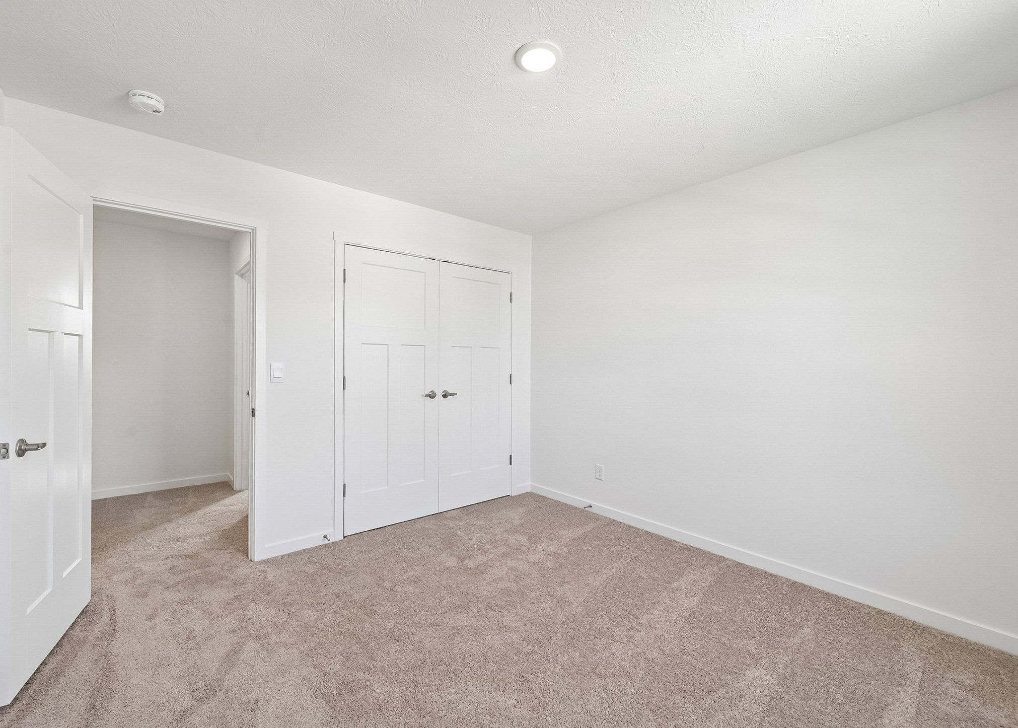 Empty room with beige carpet, two doors leading to adjacent spaces, and plain white walls.