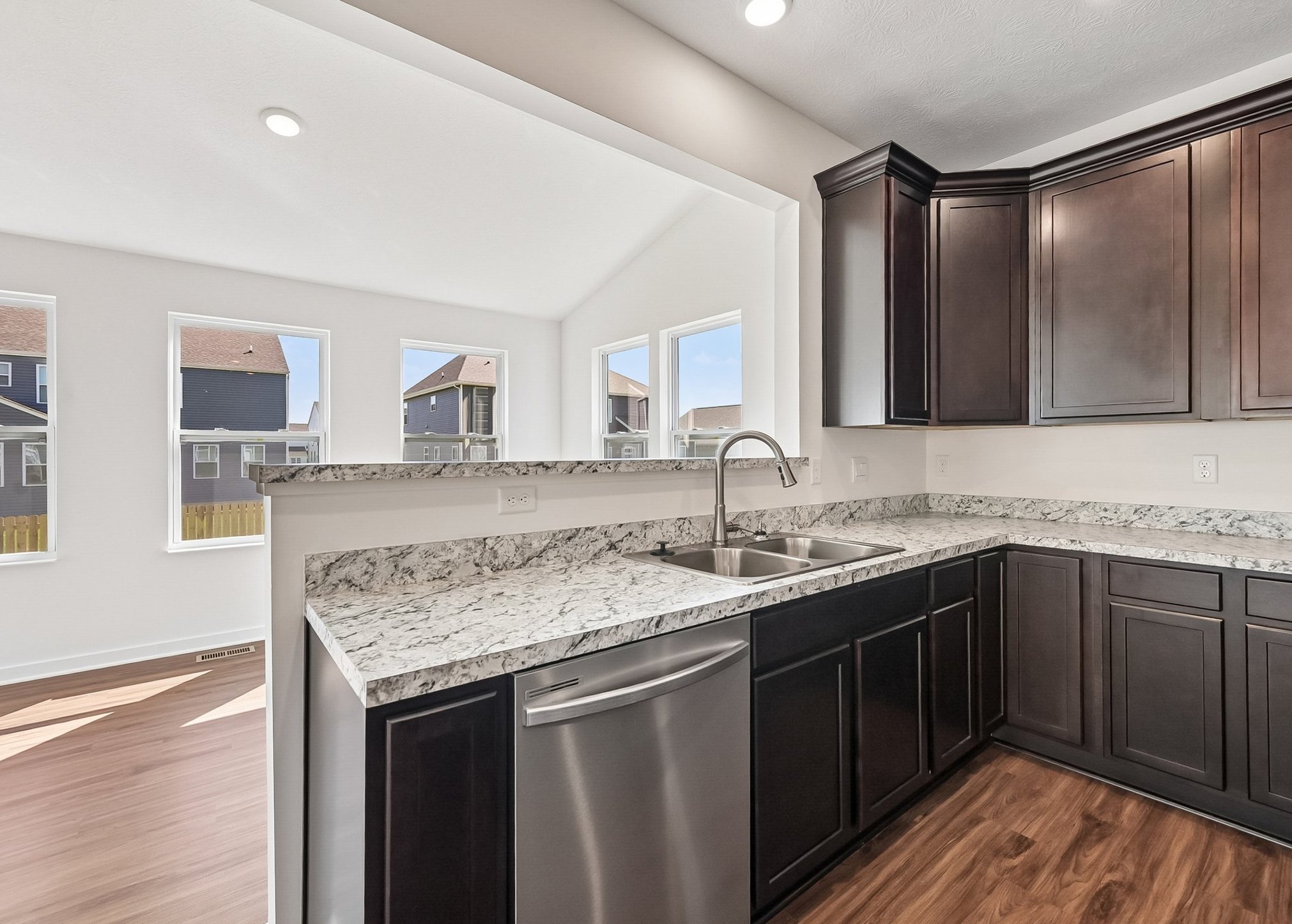 A modern kitchen with dark cabinetry, granite countertops, a stainless steel sink, and large windows letting in natural light.