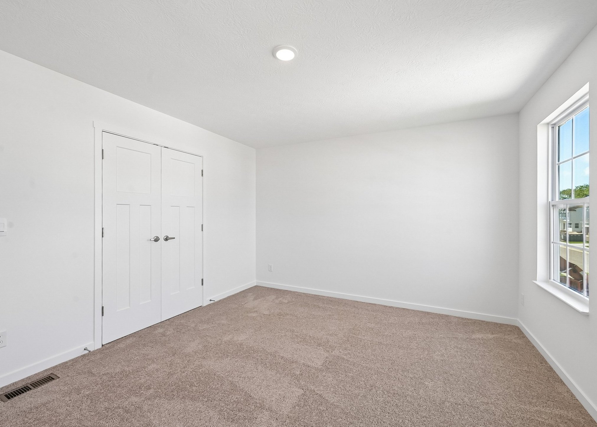 Empty room with light-colored walls, a carpeted floor, a window, and double doors.