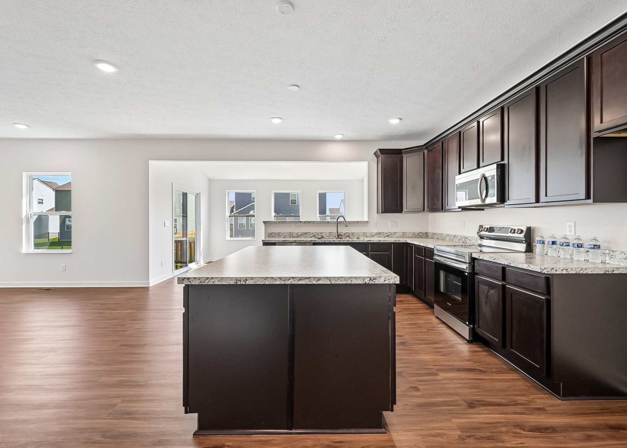 Modern kitchen featuring dark cabinets, granite countertops, and stainless steel appliances, with large windows allowing natural light.