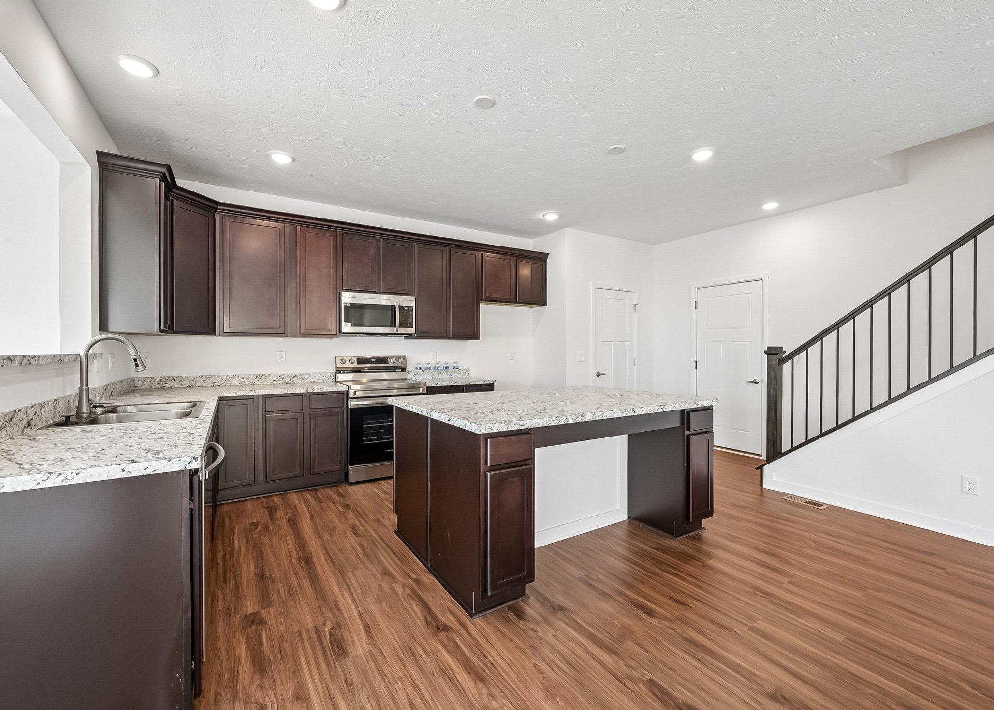 Modern kitchen with dark wood cabinetry, granite countertops, and stainless steel appliances, featuring a central island and open floor plan.