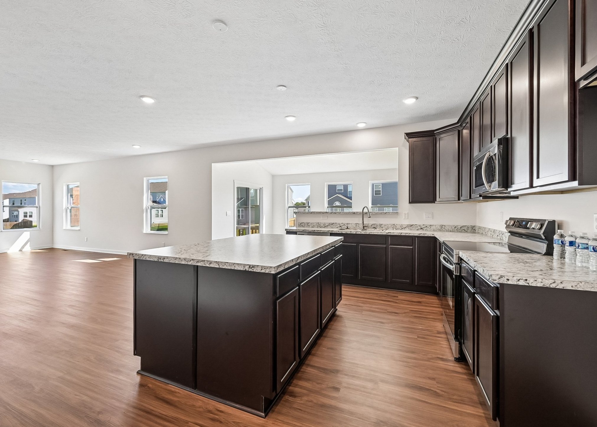 Modern kitchen featuring dark wood cabinetry, a spacious island with a granite countertop, and large windows allowing natural light.