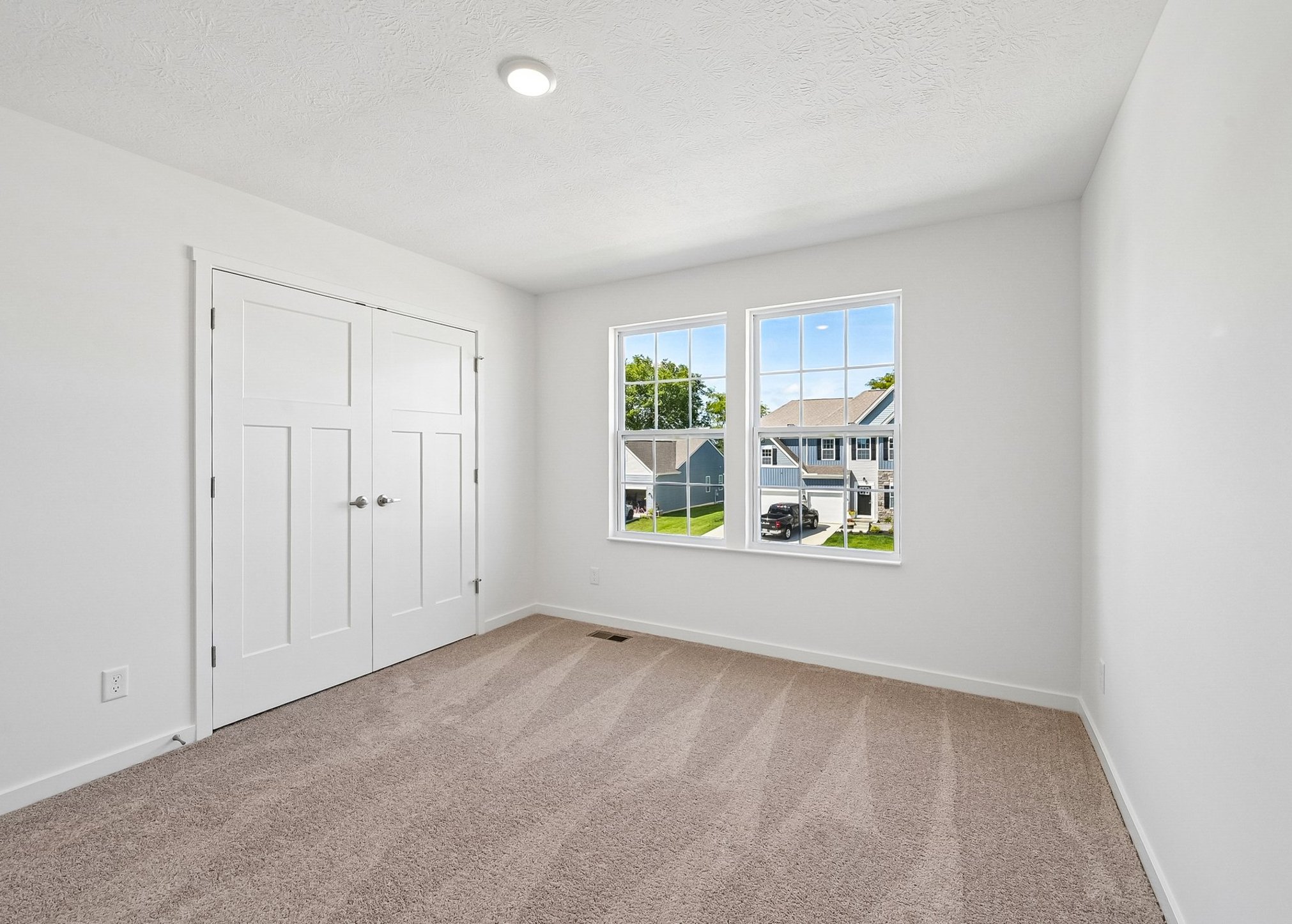 Bright, empty room with beige carpet, two windows, and white double doors.