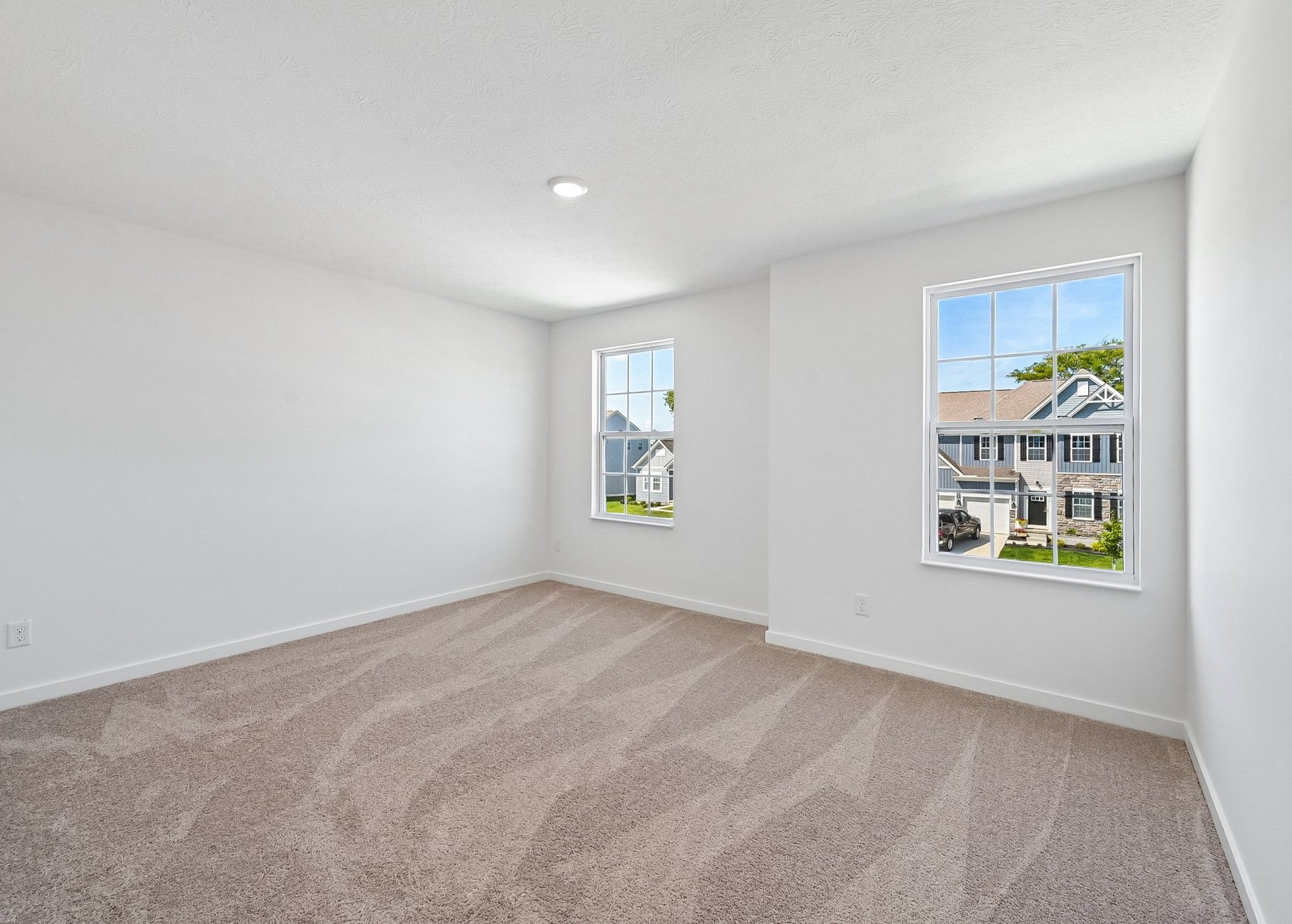 A spacious, empty room with light grey walls and two large windows letting in natural light.