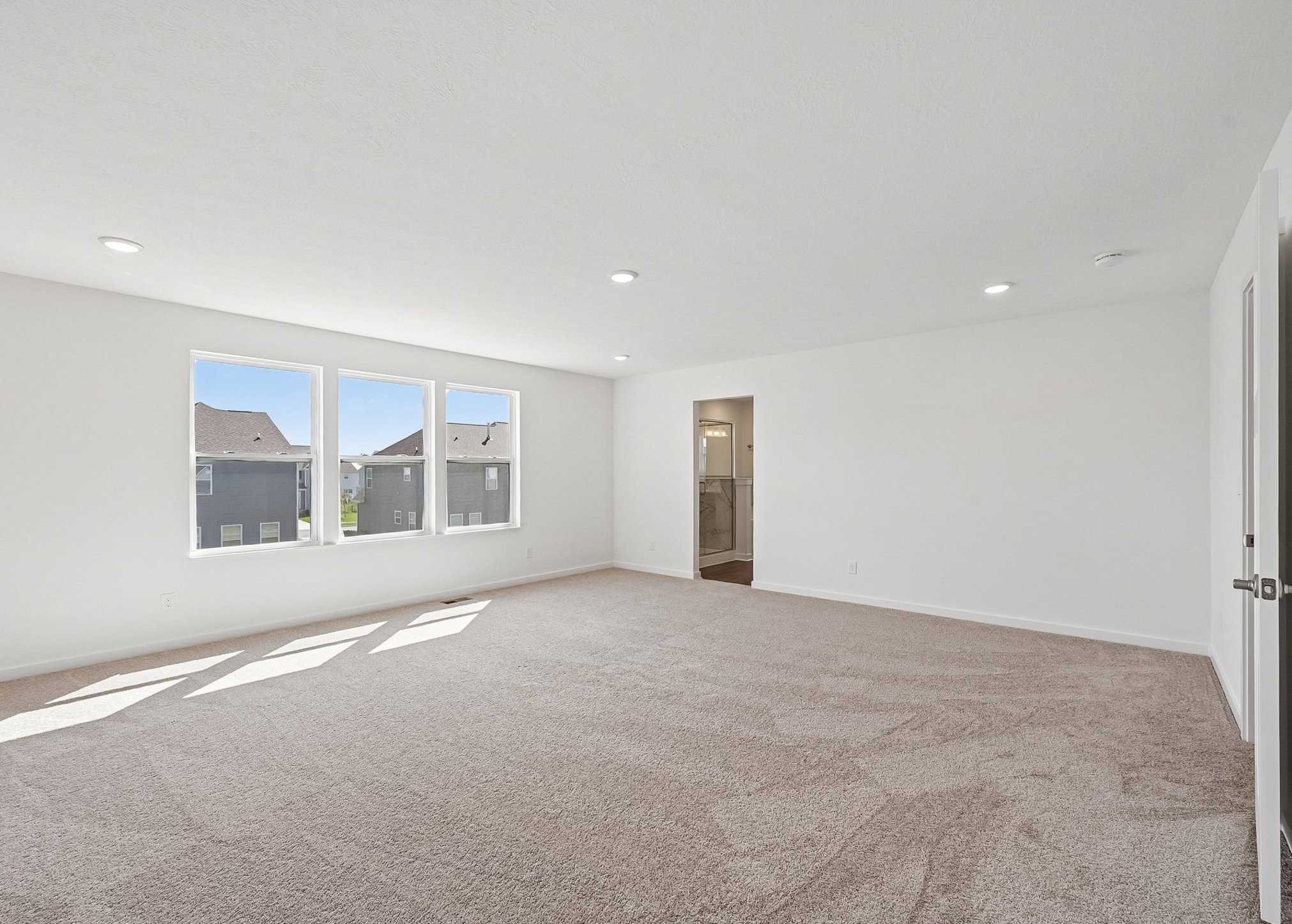 Spacious, empty room with beige carpet and large windows allowing natural light.