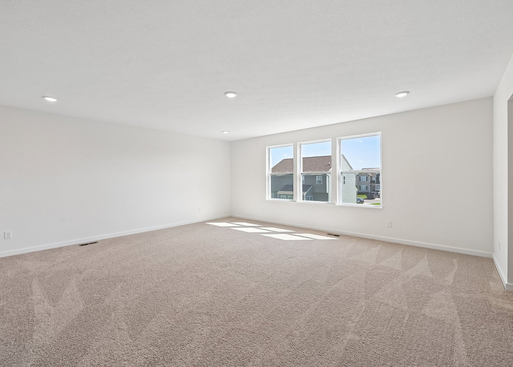 Spacious, empty room with carpet flooring and large windows letting in natural light.