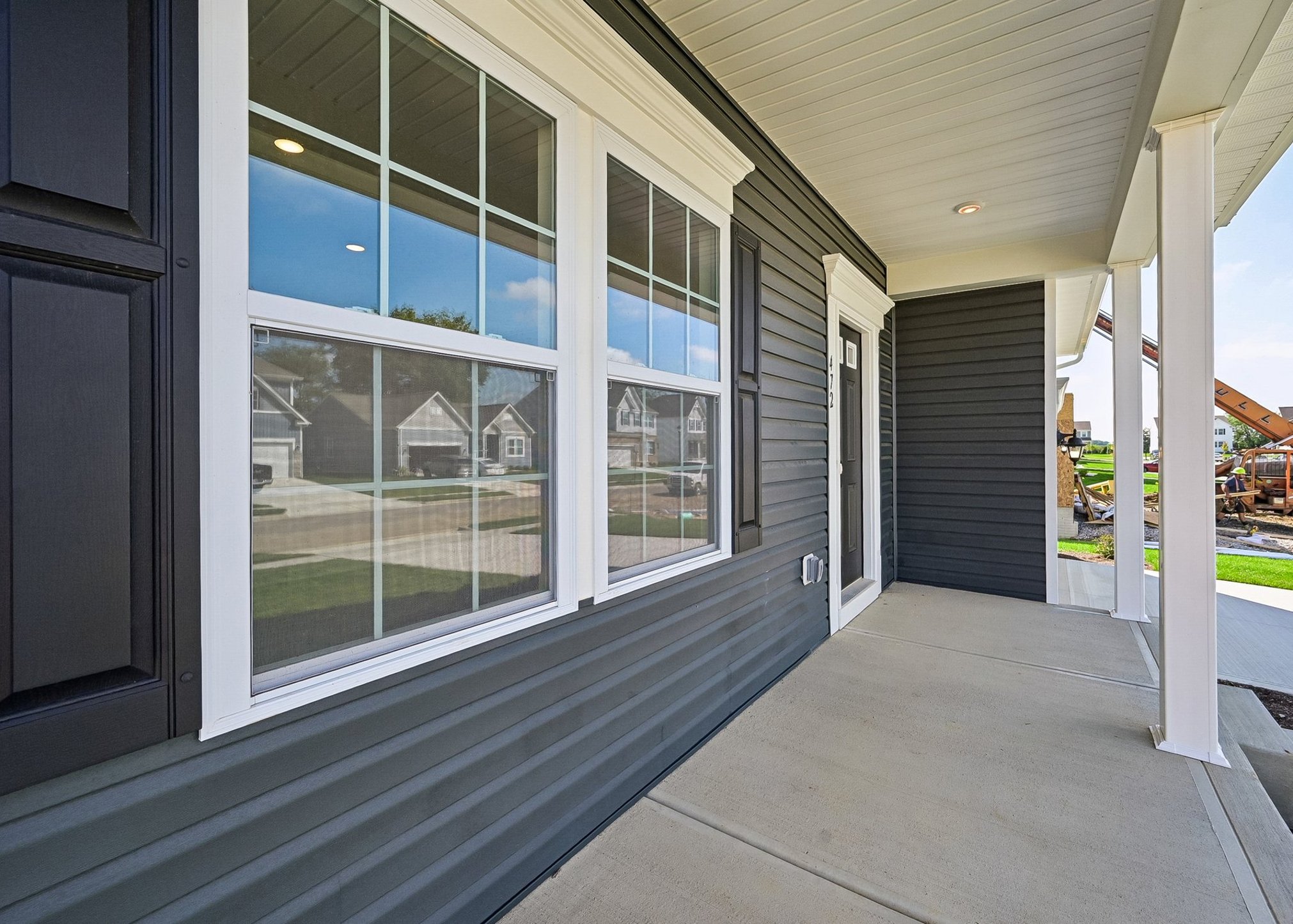 Front porch of a house featuring gray siding and large windows reflecting the neighborhood.