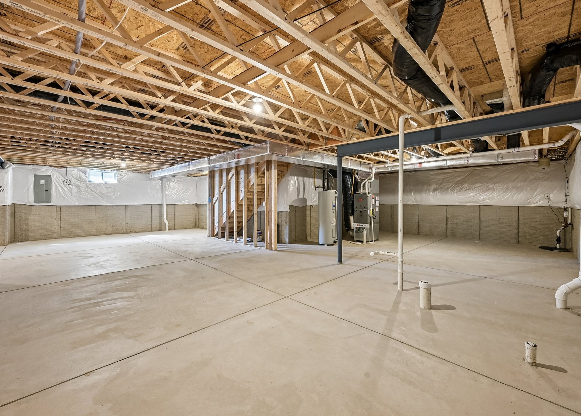 A spacious, unfinished basement with exposed wooden beams and concrete flooring.