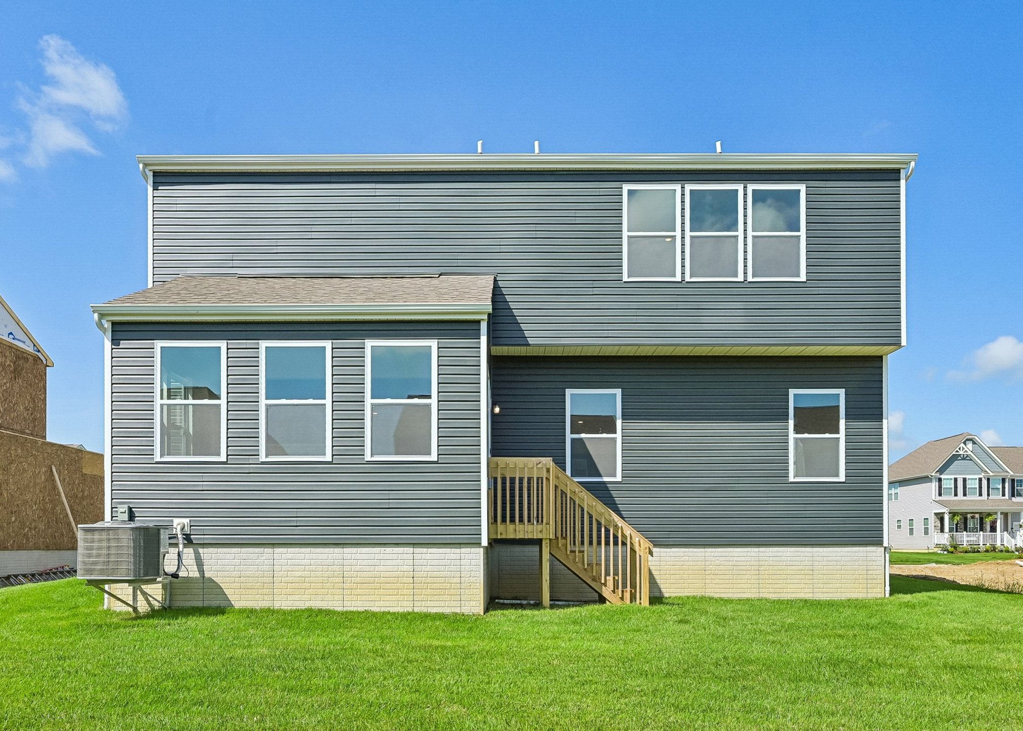 Two-story gray house with multiple windows and a wooden staircase leading to the backyard, situated on a grassy lawn.