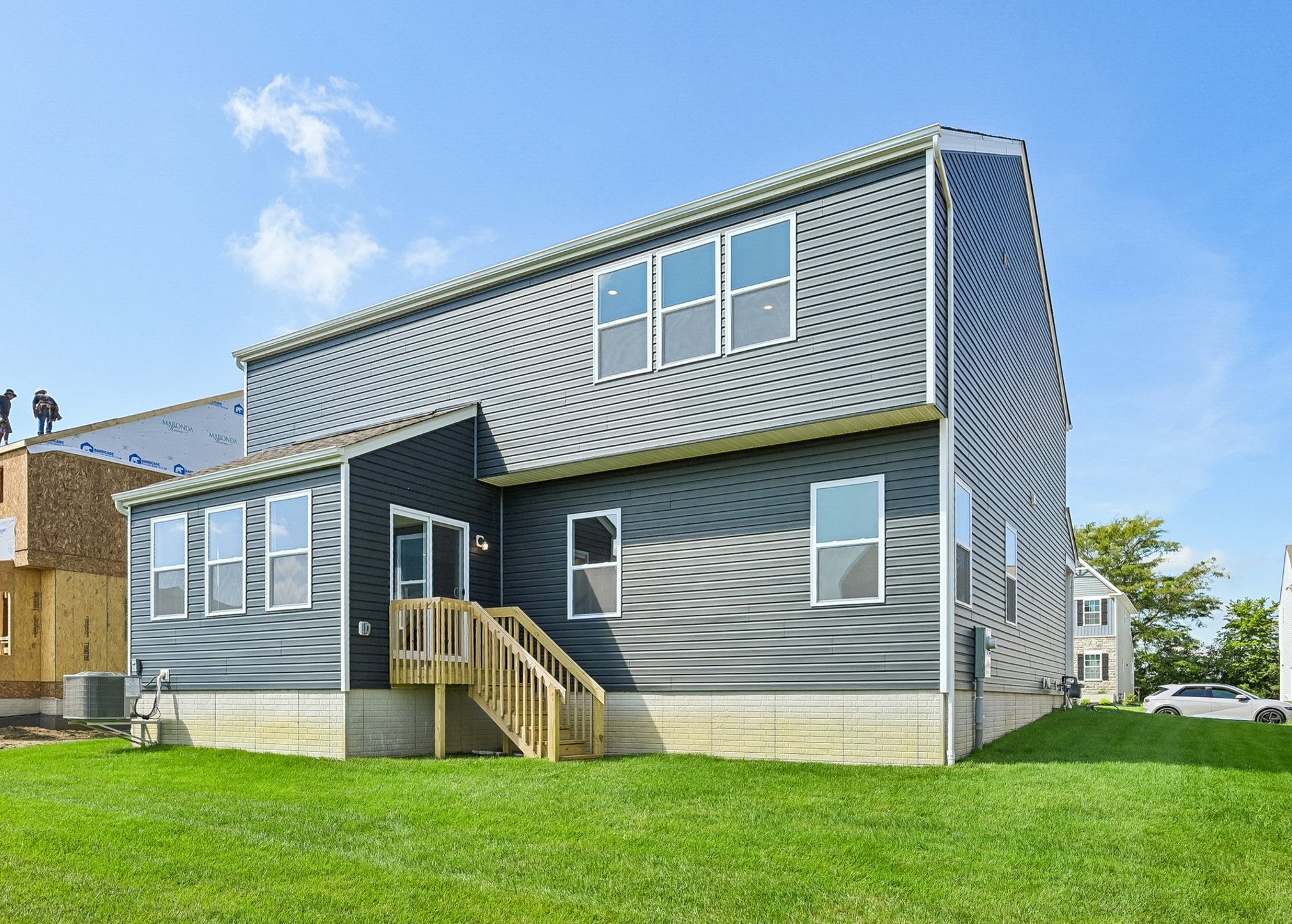 Modern gray house with multiple windows and a wooden staircase, situated on a grassy lawn.