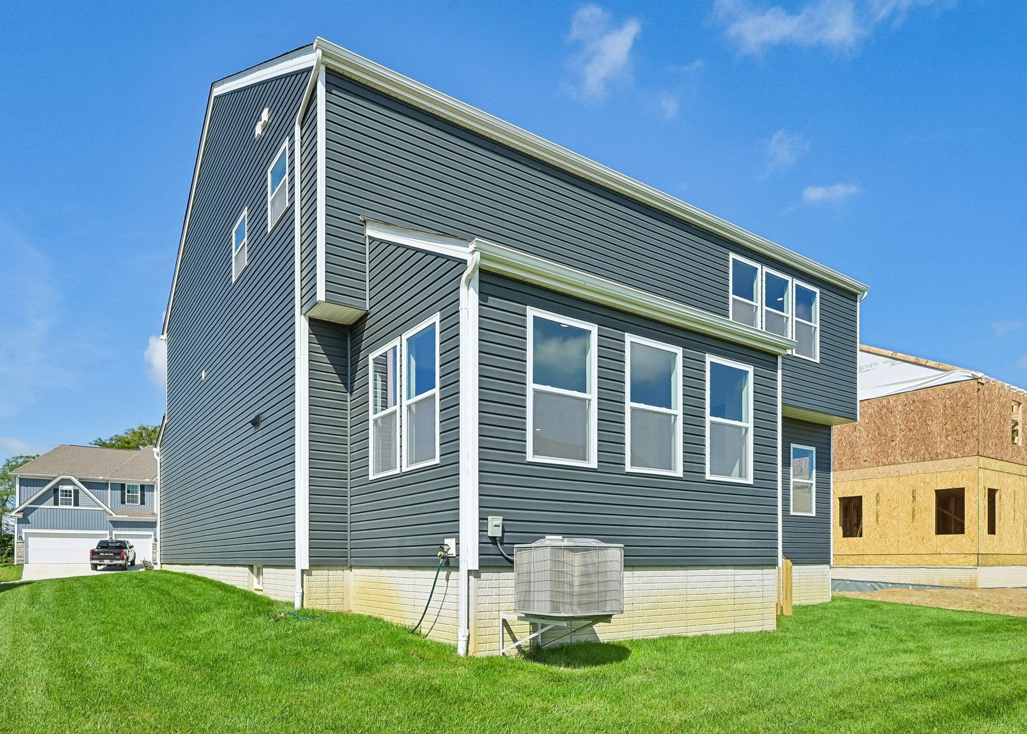 A modern gray house with large windows, sitting on a green lawn next to a partially constructed building.