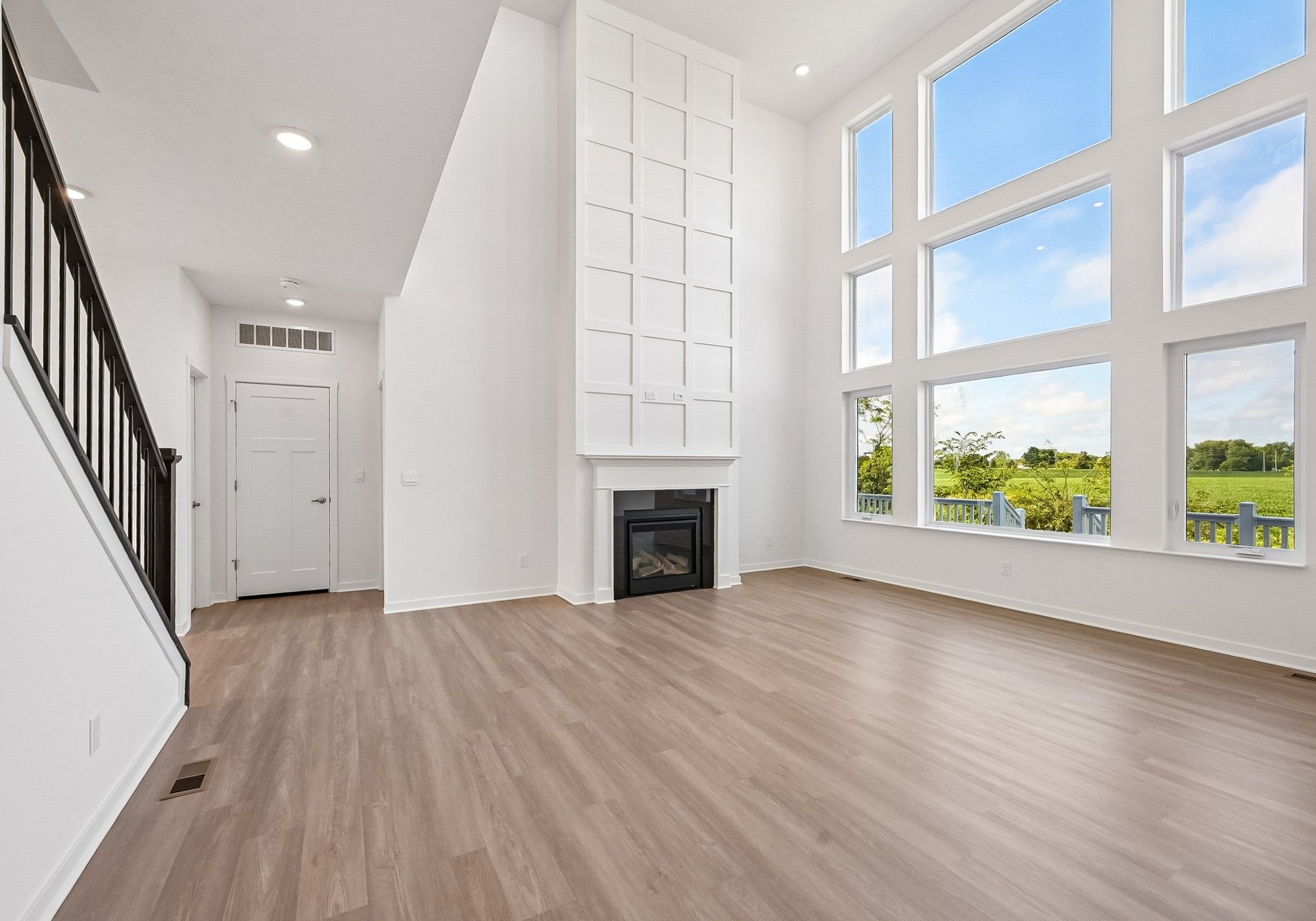 Spacious modern living room with tall windows, light wood flooring, and a fireplace.