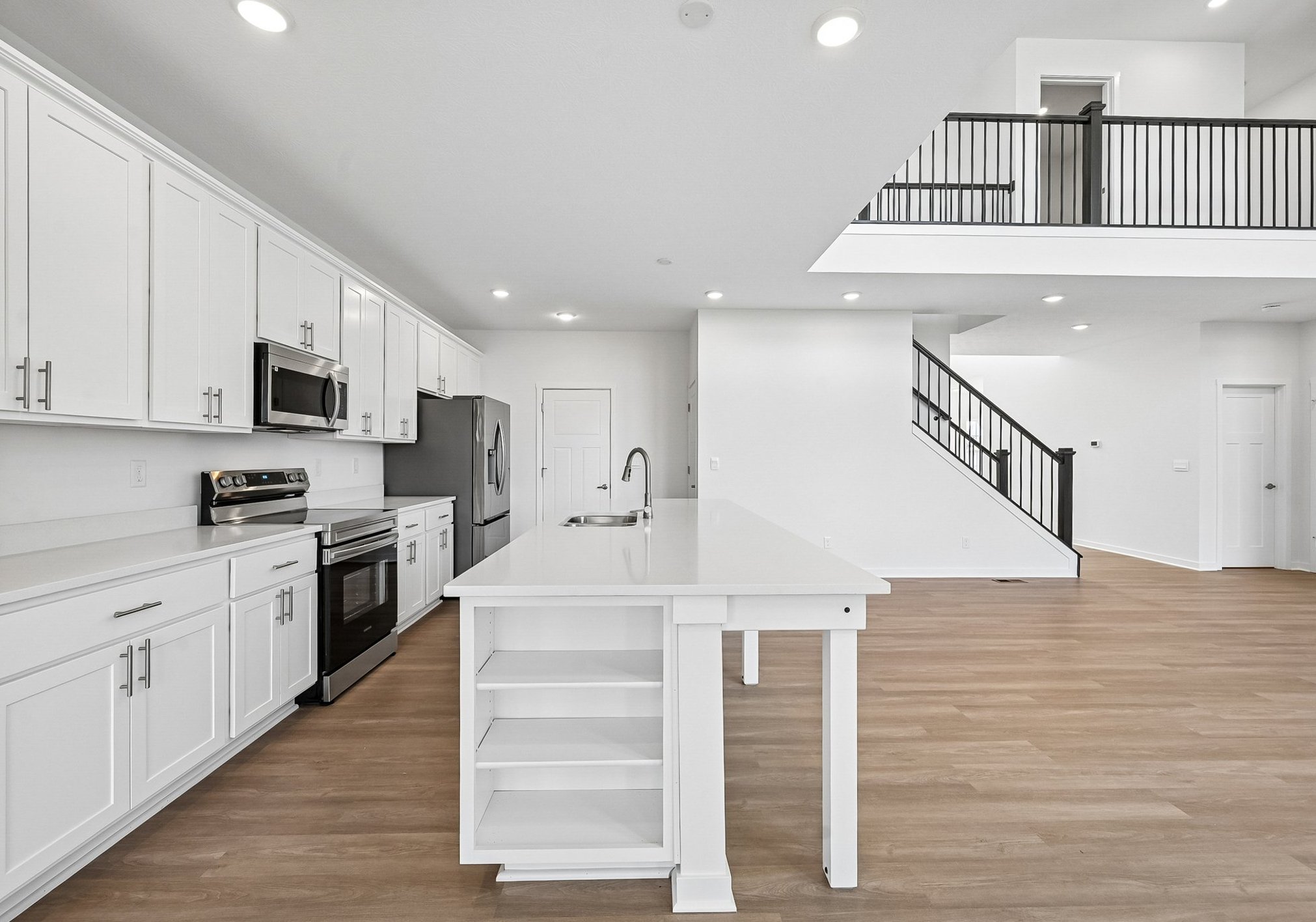 Modern kitchen with white cabinetry, stainless steel appliances, and a large island leading to an open living space.