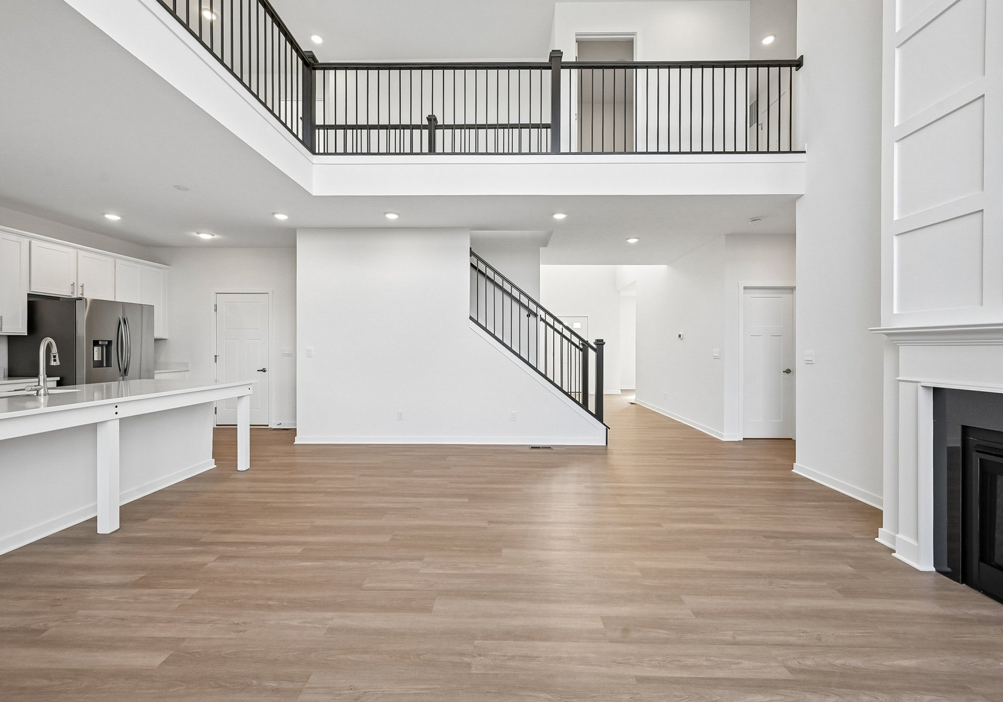 Bright, modern open-concept living space with hardwood floors, a white kitchen, and a staircase leading to an upper level.
