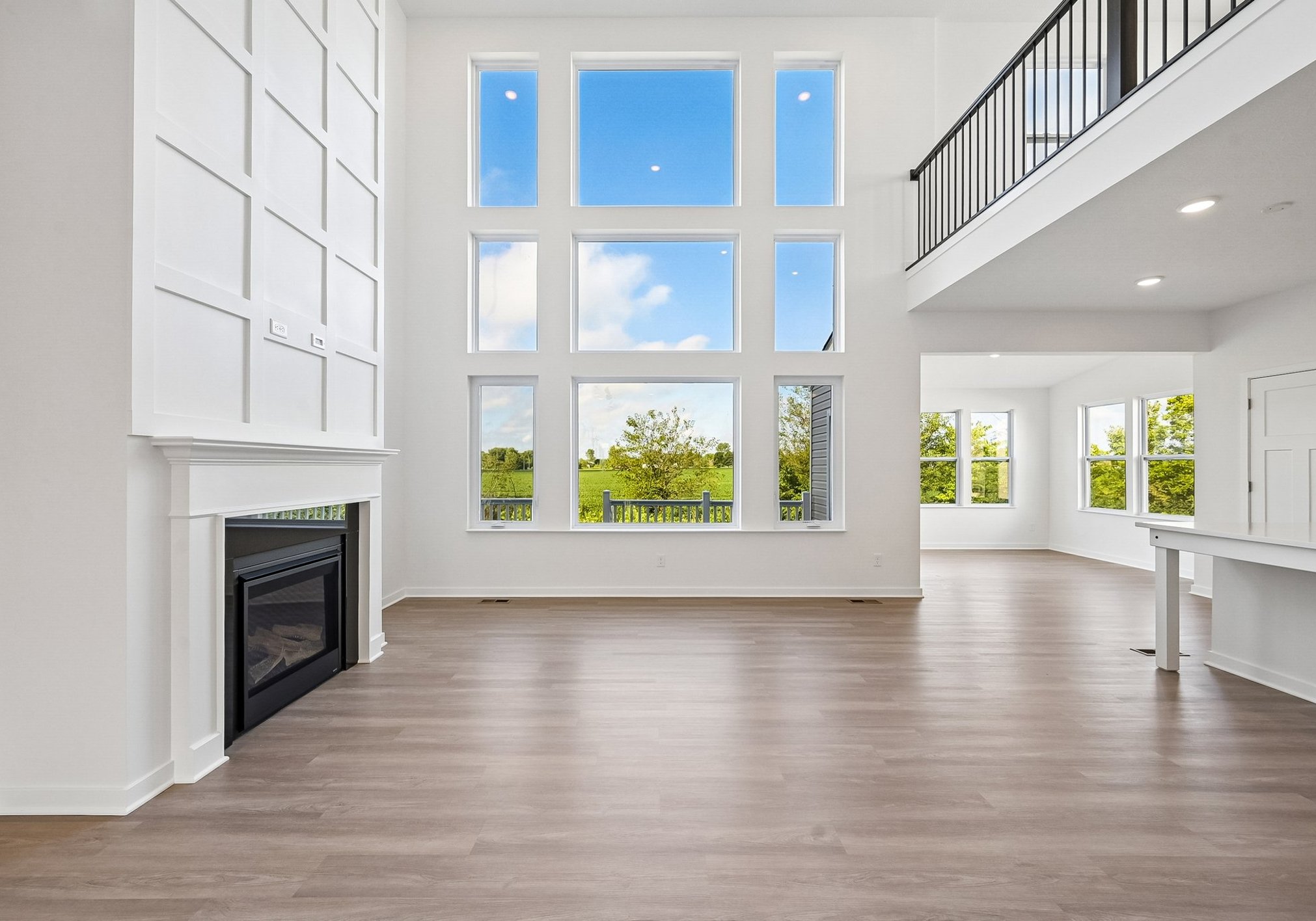 Spacious living room with large windows offering a view of greenery and a modern fireplace.