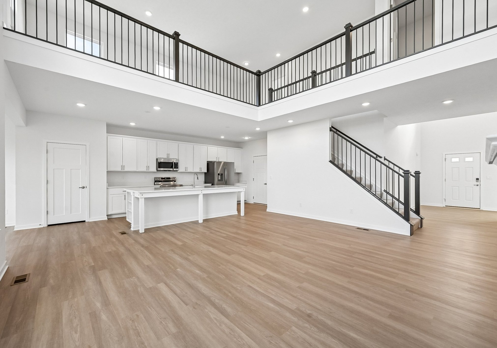 Spacious open-concept living area with a modern kitchen, hardwood flooring, and a staircase leading to a second level.