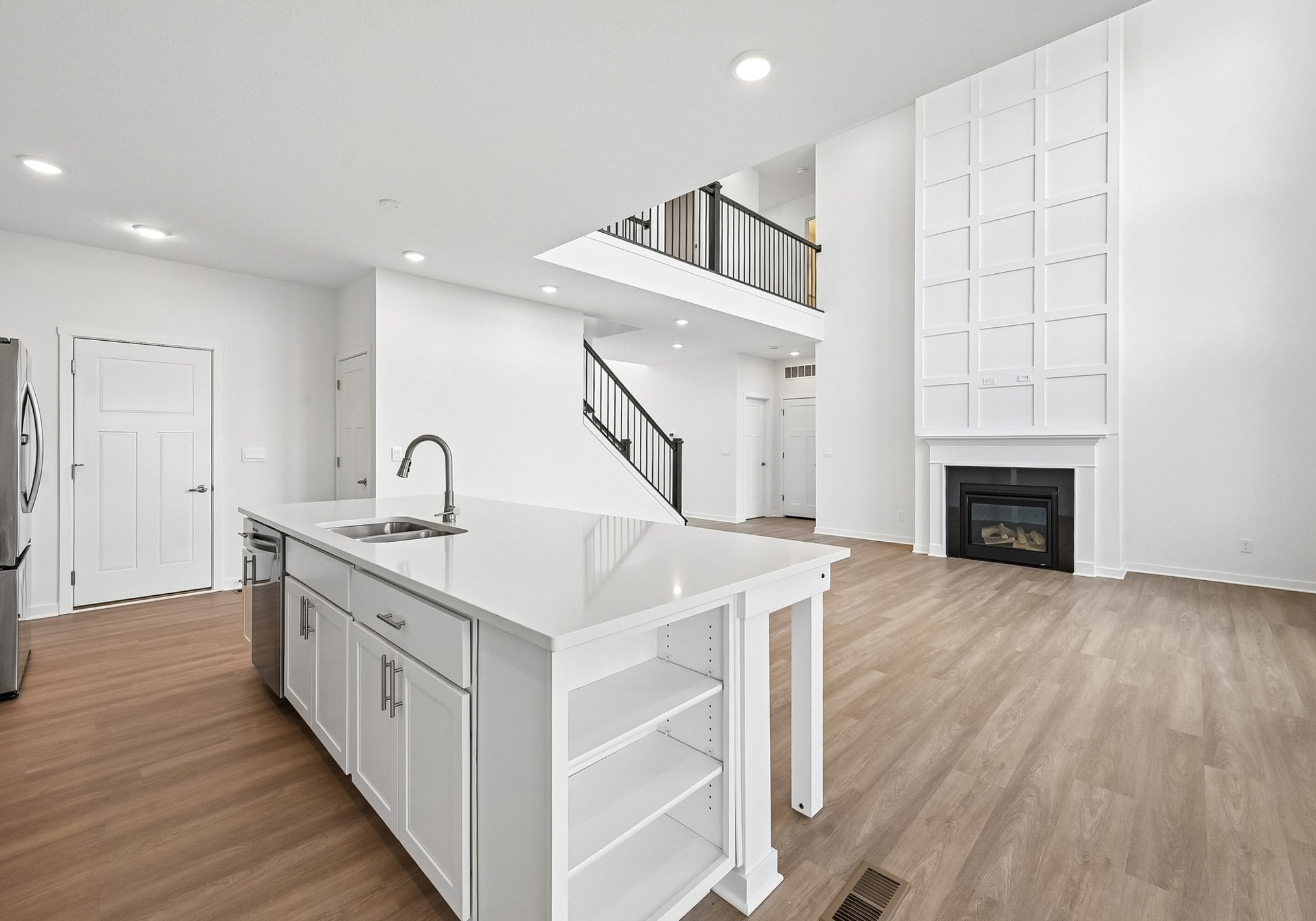 Modern open-concept living space featuring a kitchen island, hardwood flooring, and a fireplace.