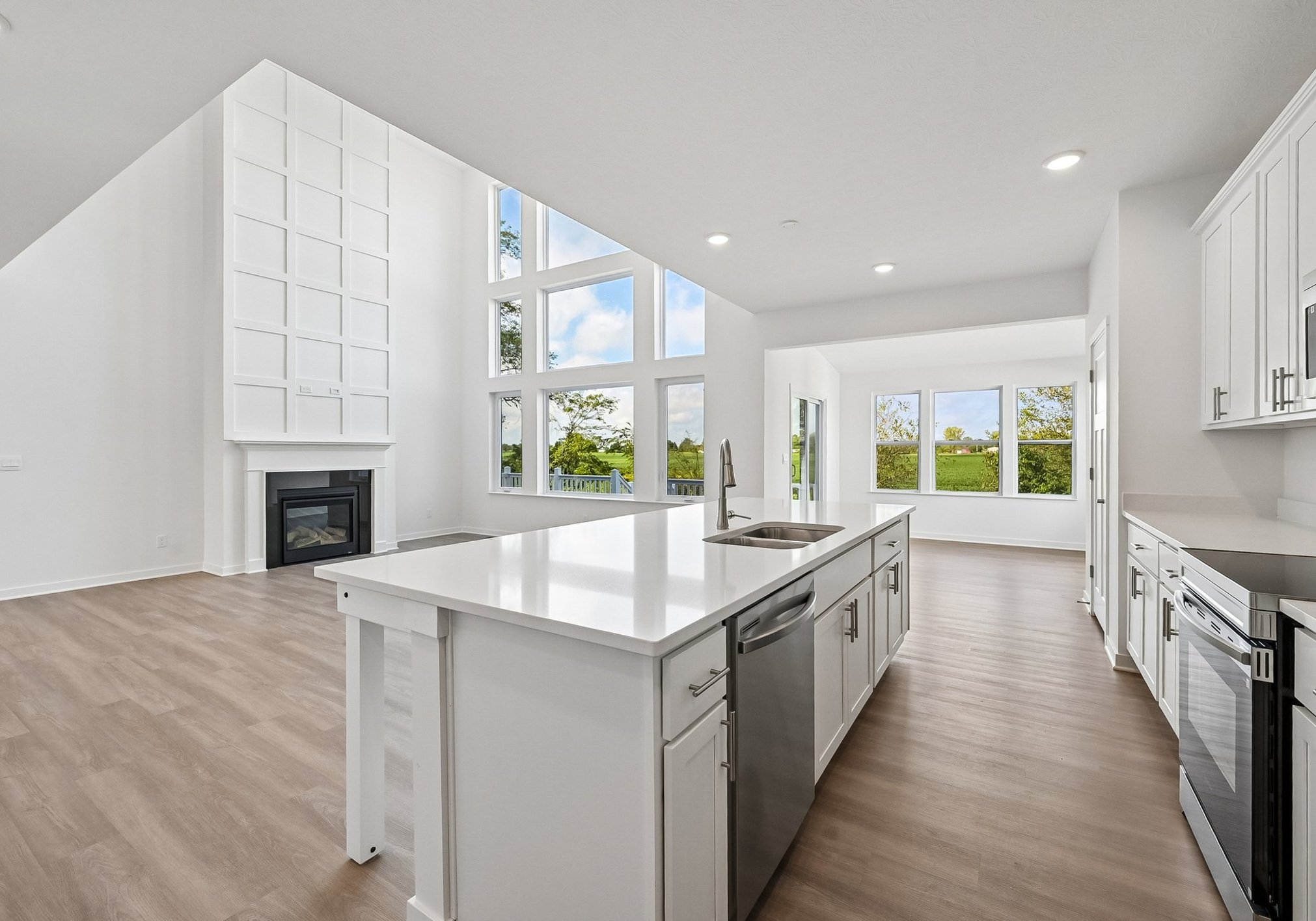 Bright modern kitchen with white cabinetry, large windows, and an open layout leading to a living area.