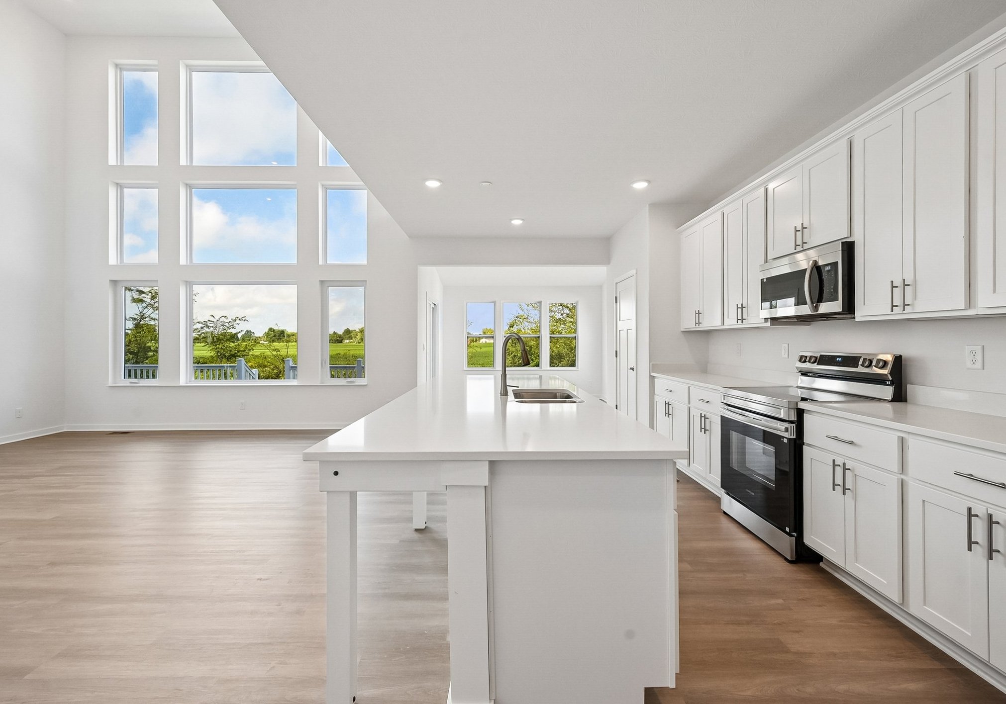 Spacious modern kitchen with white cabinets and a large island, overlooking a bright, airy living area with large windows.