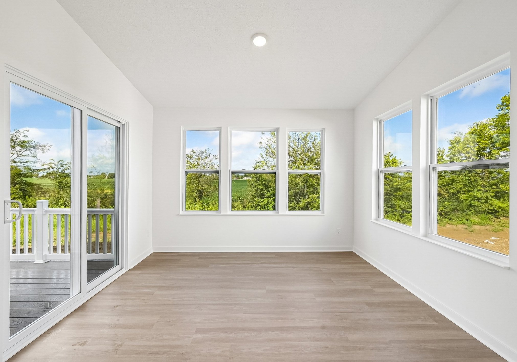 Bright, empty room with large windows offering a view of greenery outside.