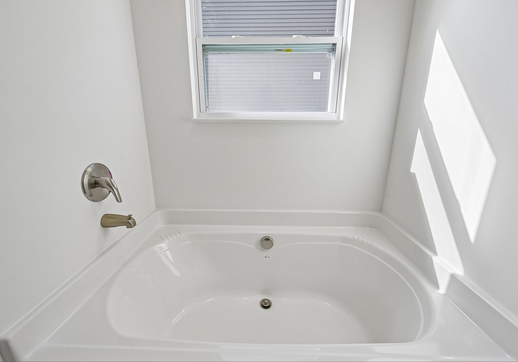 A bright, empty bathtub with a faucet and a window letting in natural light.