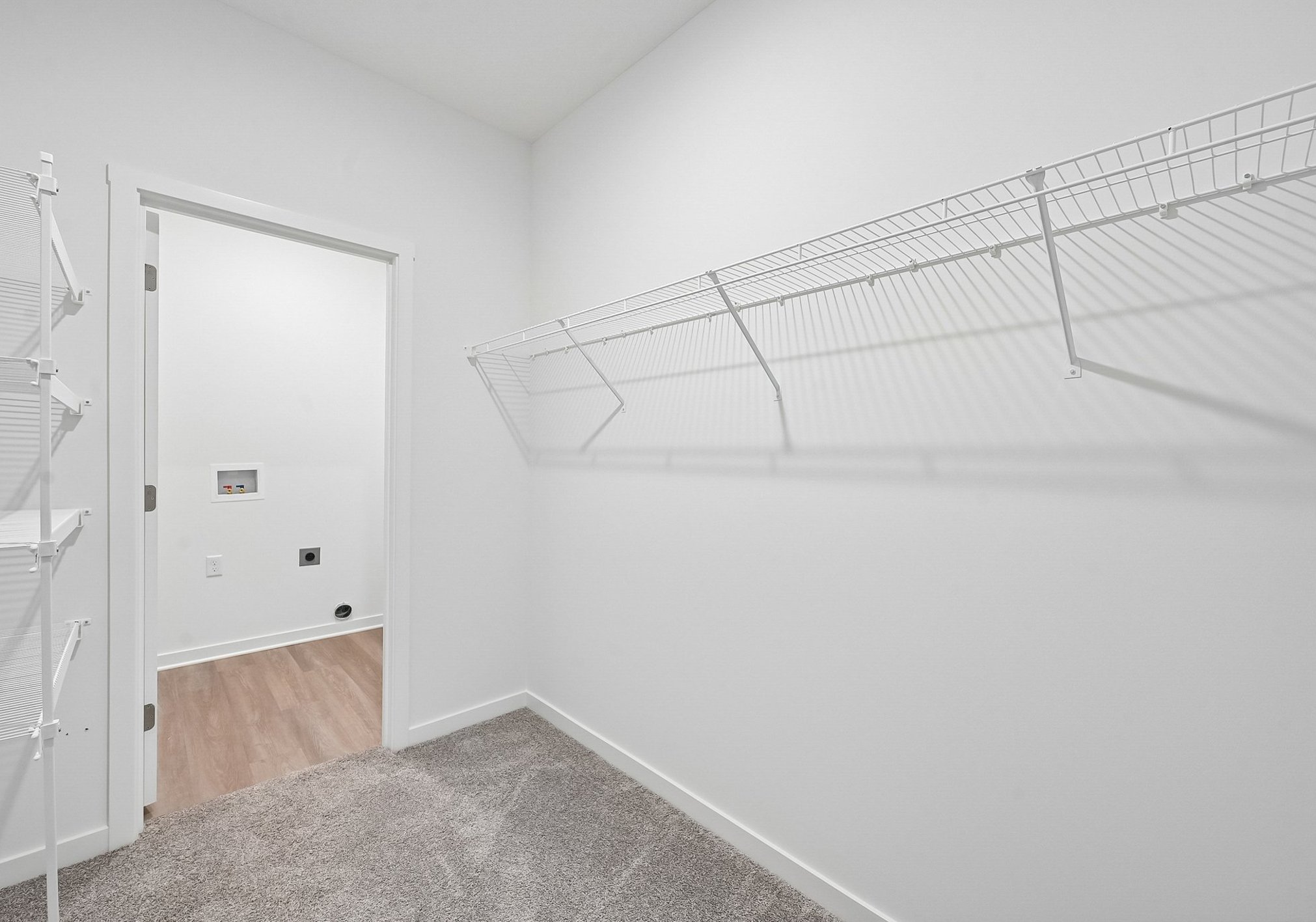 Empty room with white walls, a closet with wire shelving, and a doorway leading to another space.