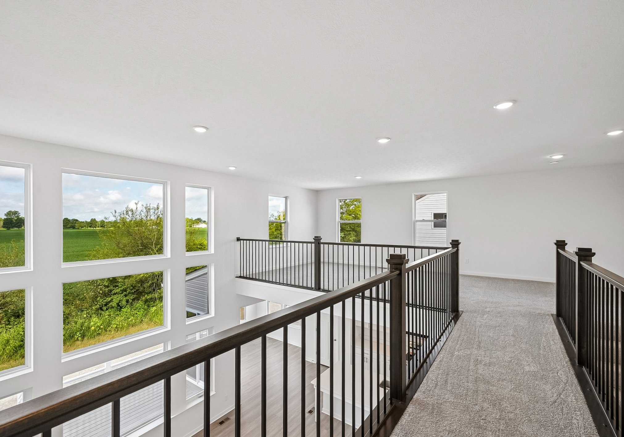 Spacious modern interior with a balcony overlooking green fields and large windows allowing natural light.