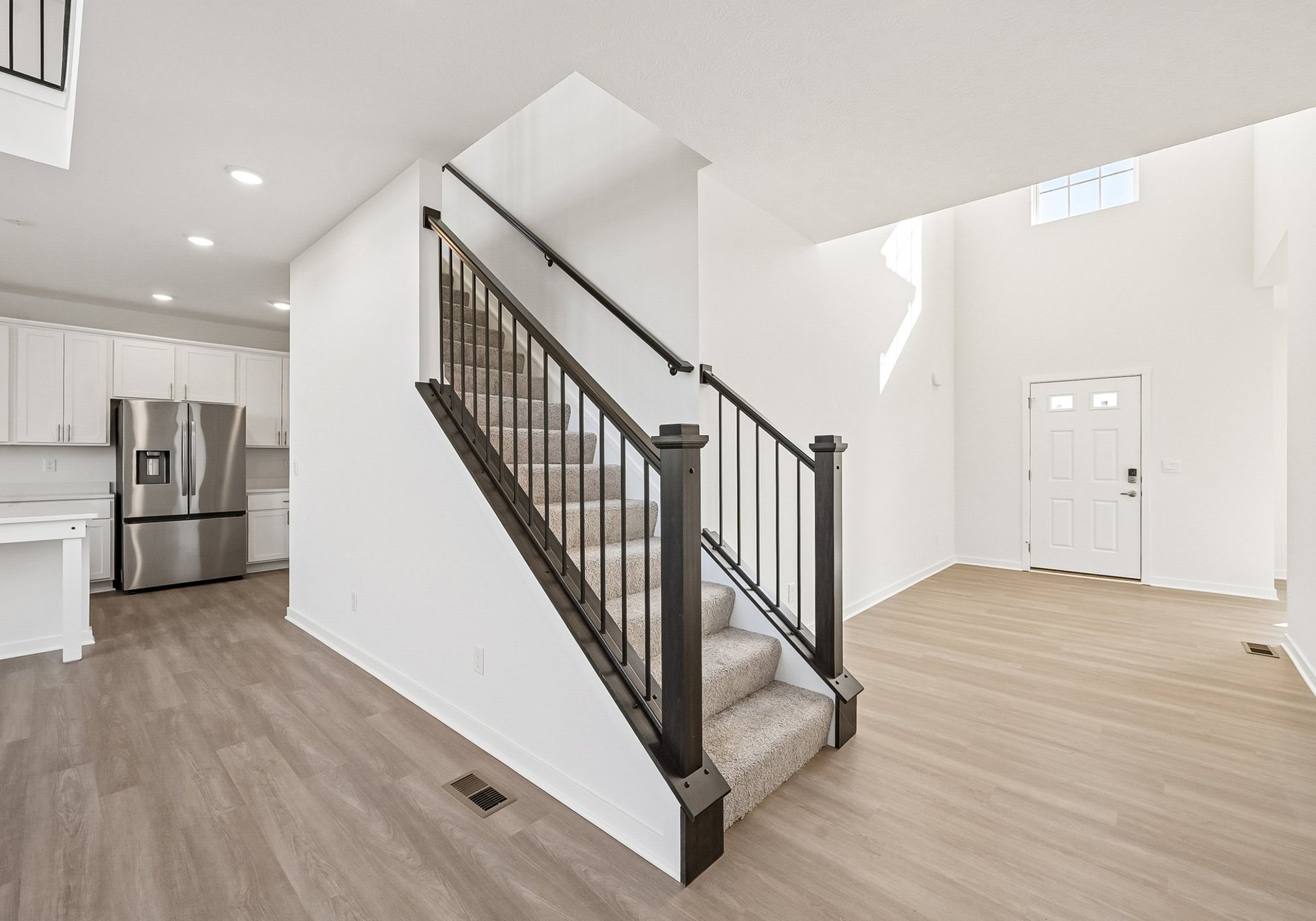 A modern entryway featuring a staircase with black railings, hardwood flooring, and a bright open space leading to a kitchen.