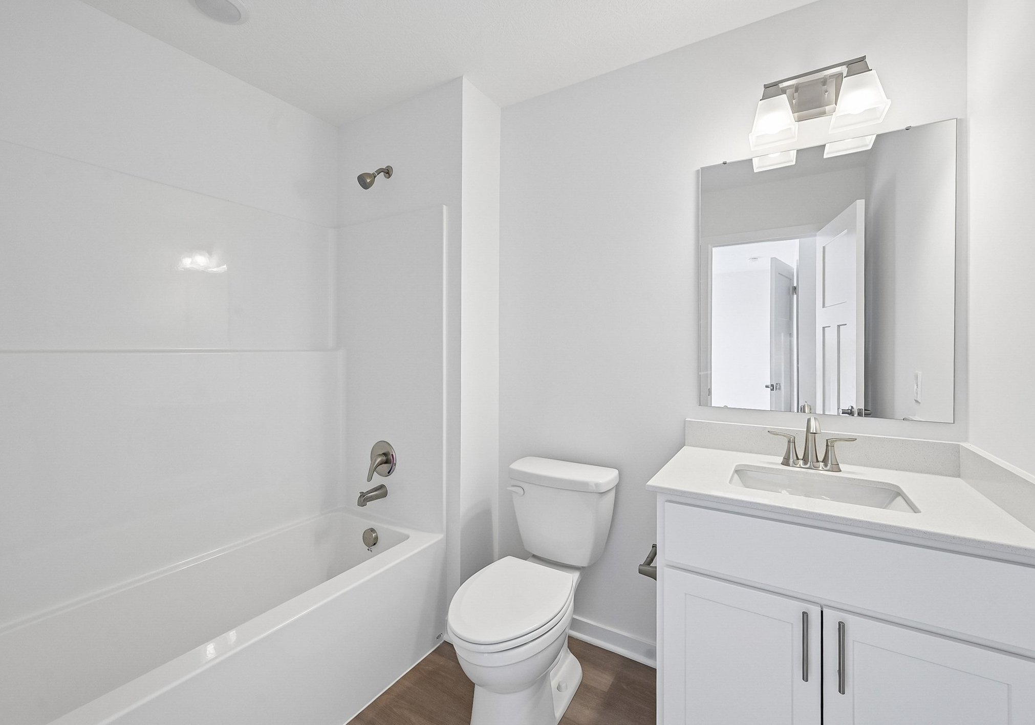 Modern bathroom featuring a bathtub, toilet, sink with a mirrored cabinet, and white walls.