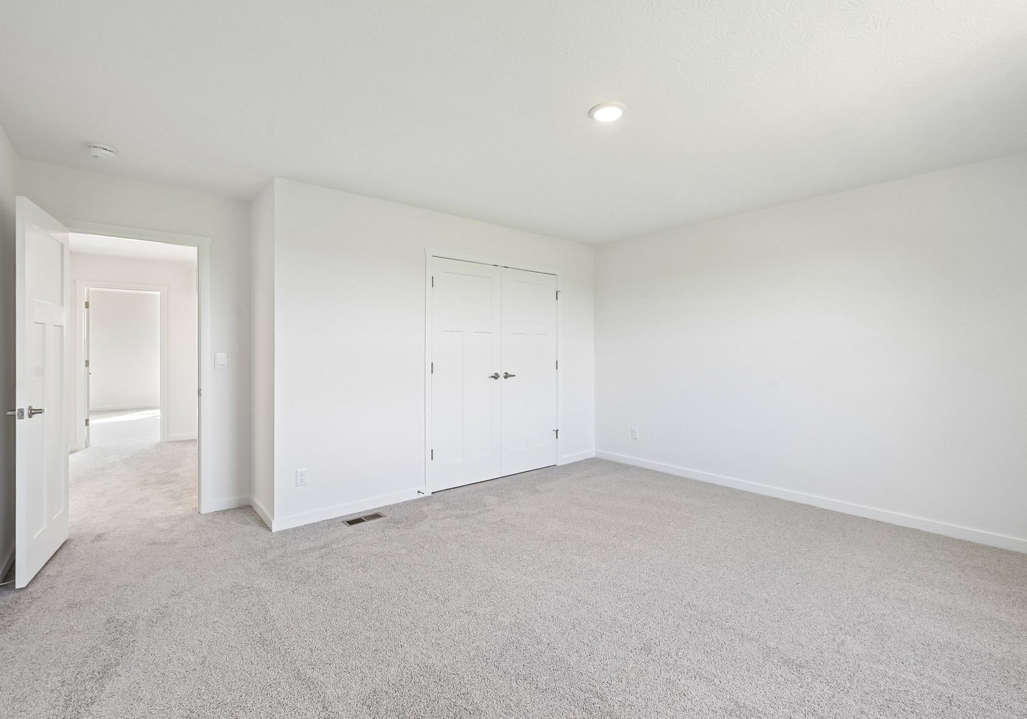 Empty room with light-colored walls, carpeted floor, and a closed closet with double doors.