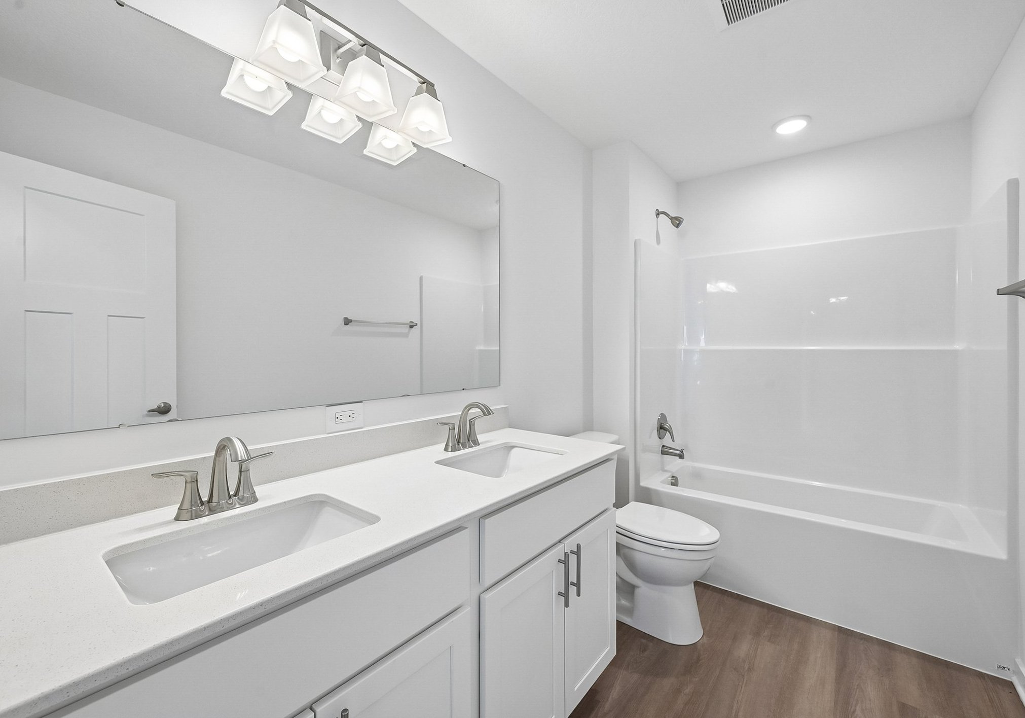 Bright, modern bathroom featuring a double sink vanity, large mirror, and a bathtub with a shower.